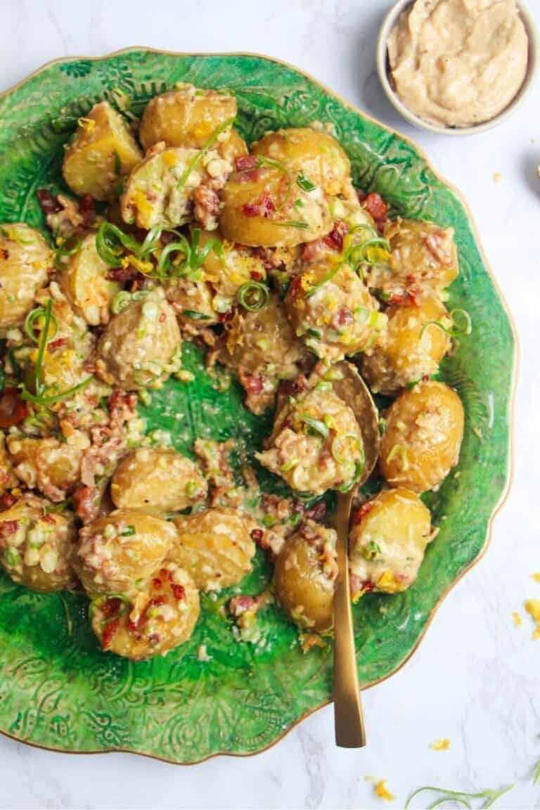 Close up of creamy Caesar potato salad on a large green serving plate with more Caesar dressing on the side.