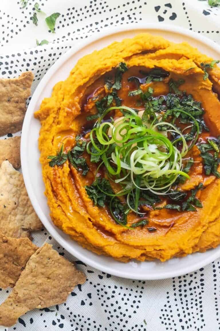 Spiced roasted carrot dip on a white and black patterned background with crackers on the side.