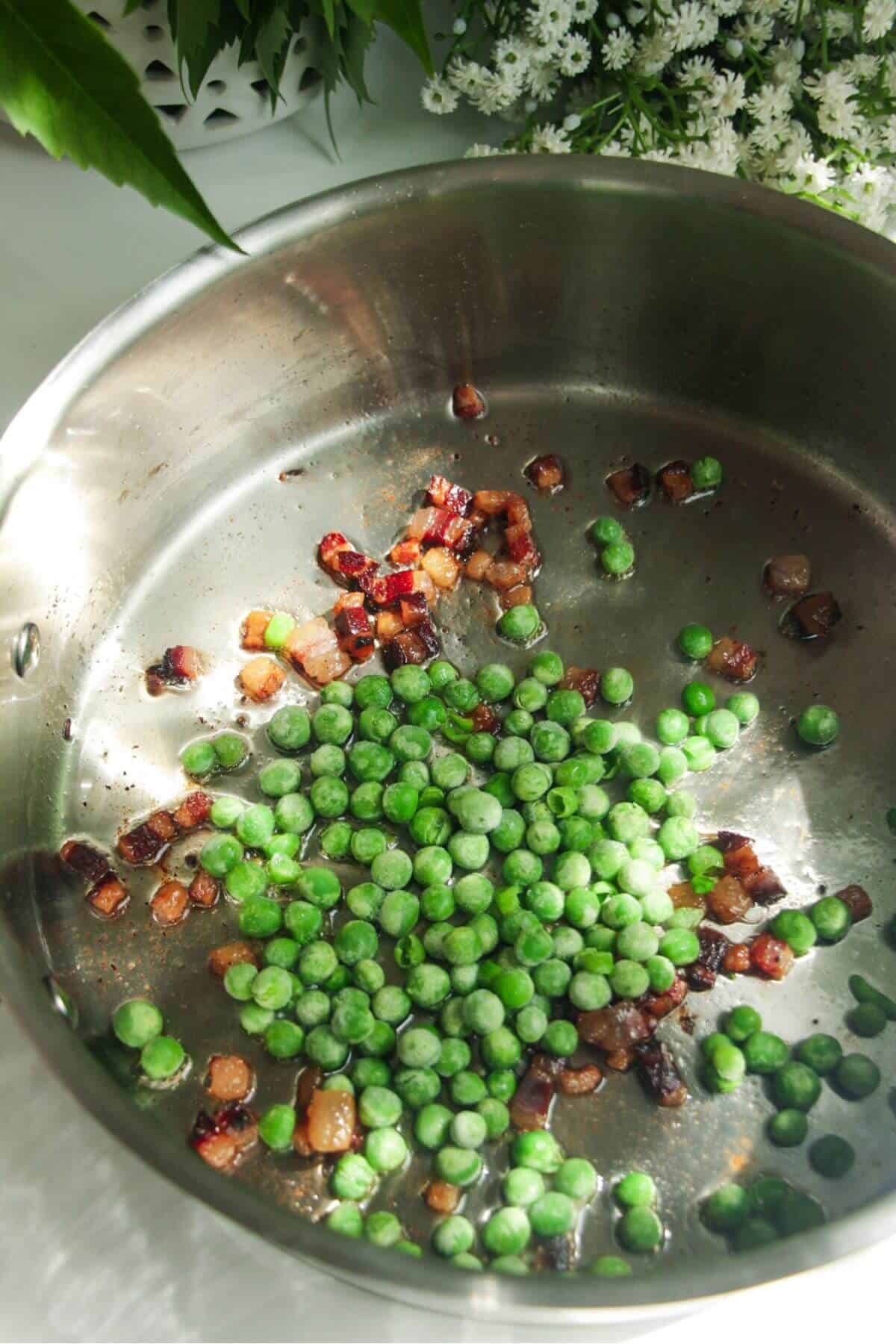 Crispy pancetta and peas in a silver pan.