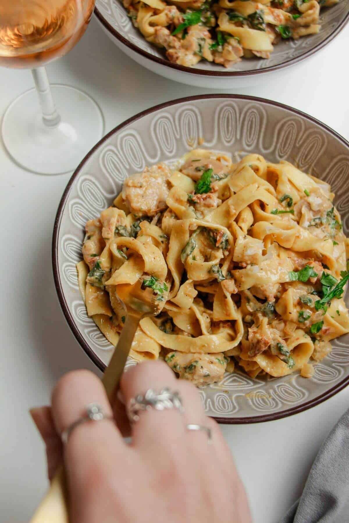 Hand twirling fork through a bowl of colourful fettuccine.