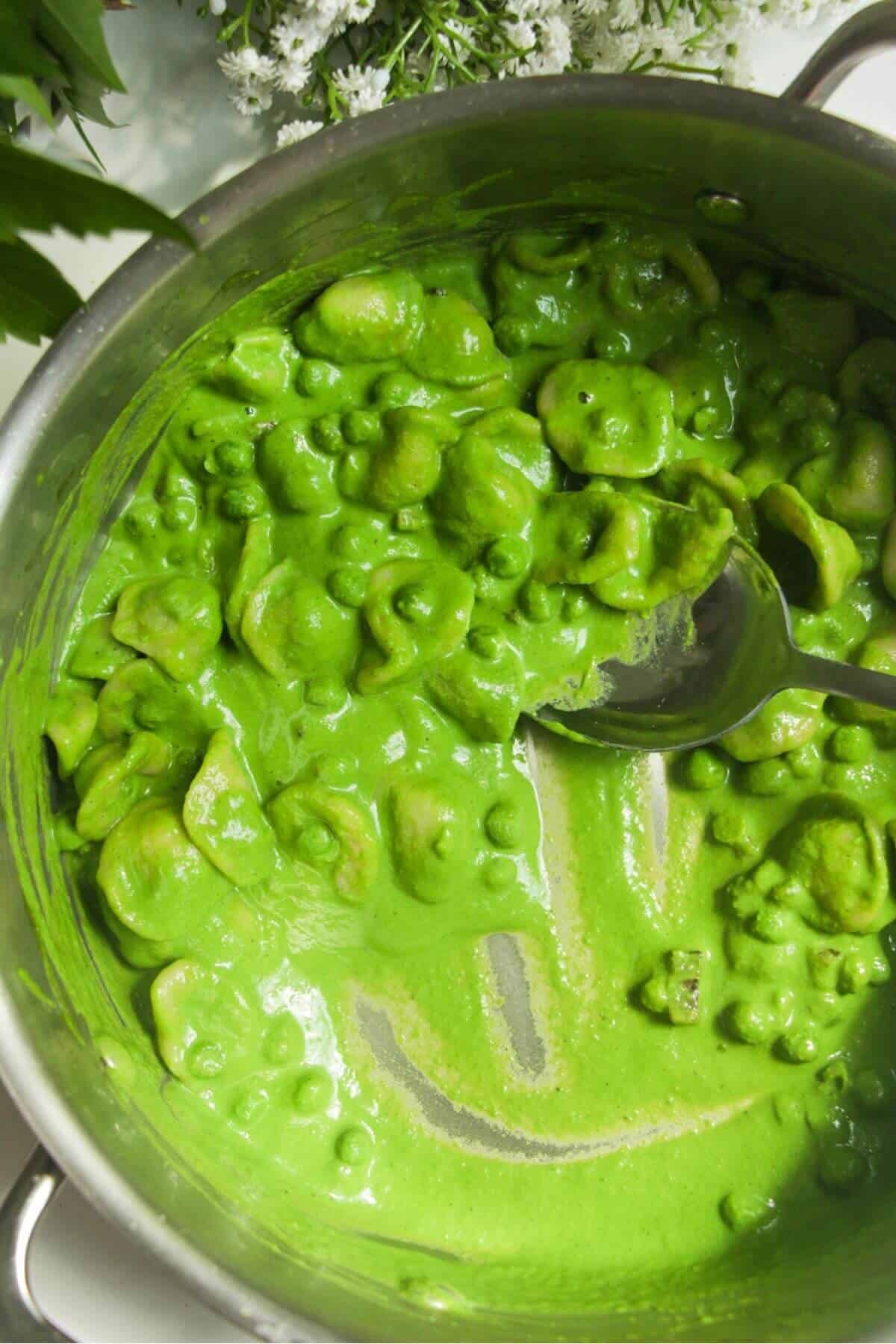 Spinach basil sauce mixed through peas, pancetta and pasta in a pan.