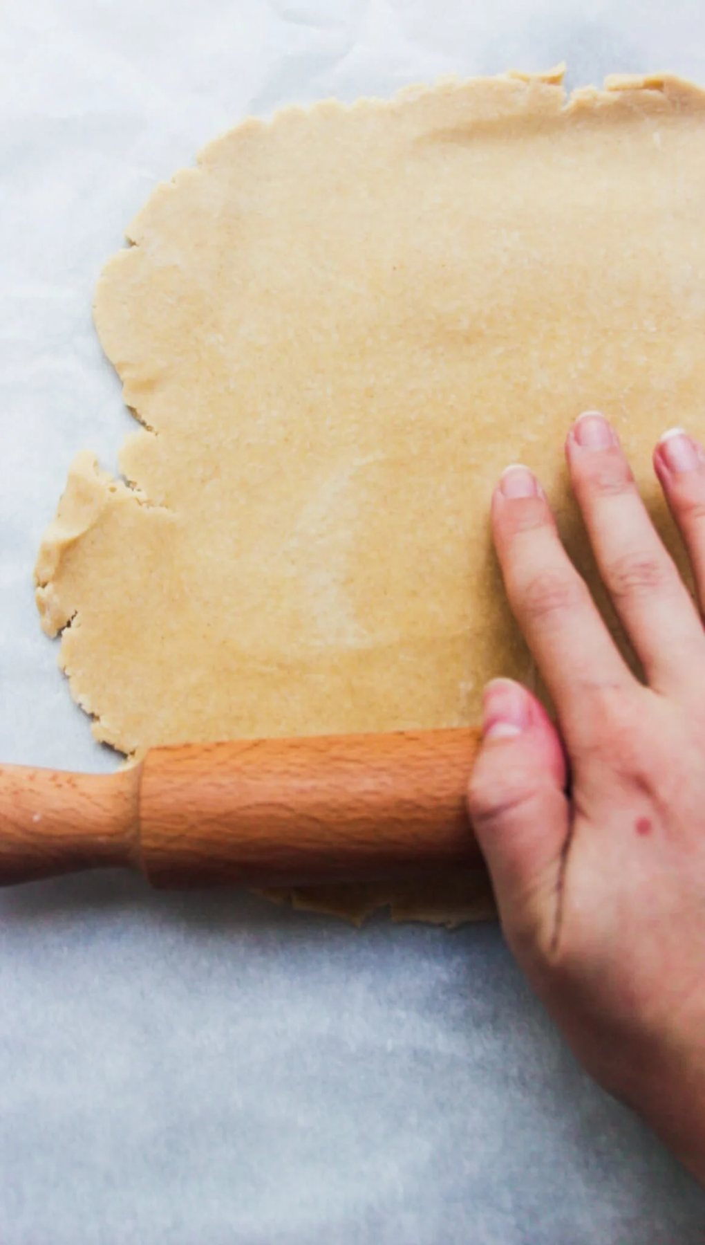 Hand and rolling pin rolling out pastry on baking paper.