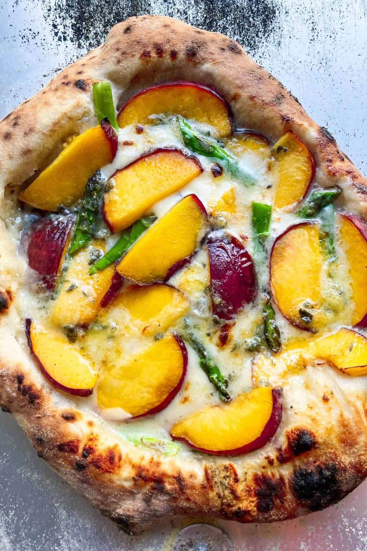 Close up of cooked peach, asparagus and blue cheese pizza on steel pizza peel.