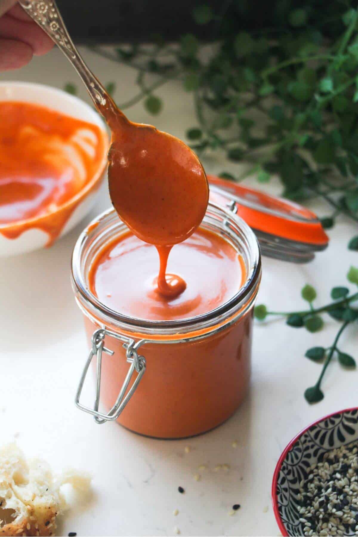 Gochujang mayo in a small glass jar with a bowl of more mayo in the background.
