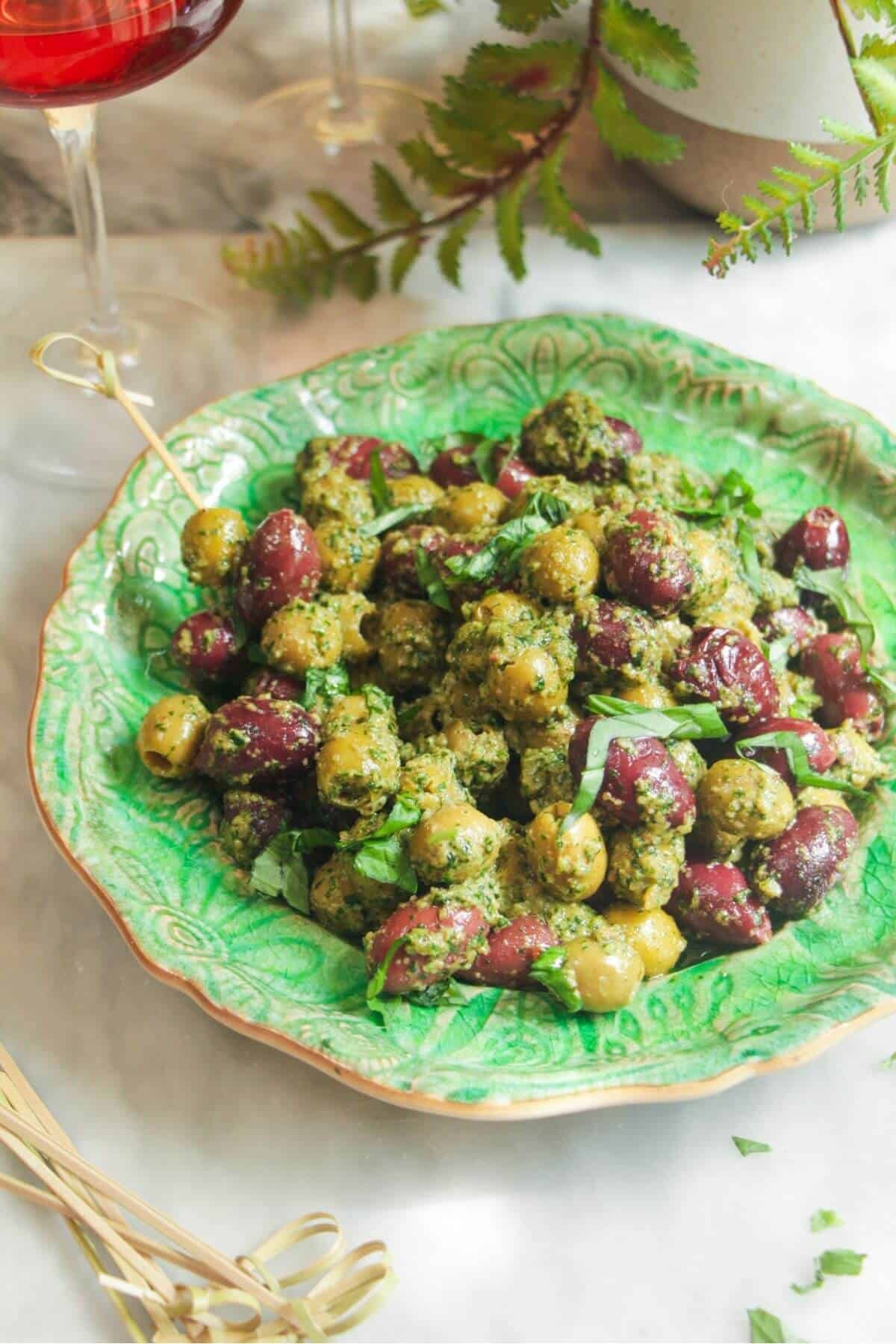 Pesto marinated olives on a small green plate with skewers on the side.