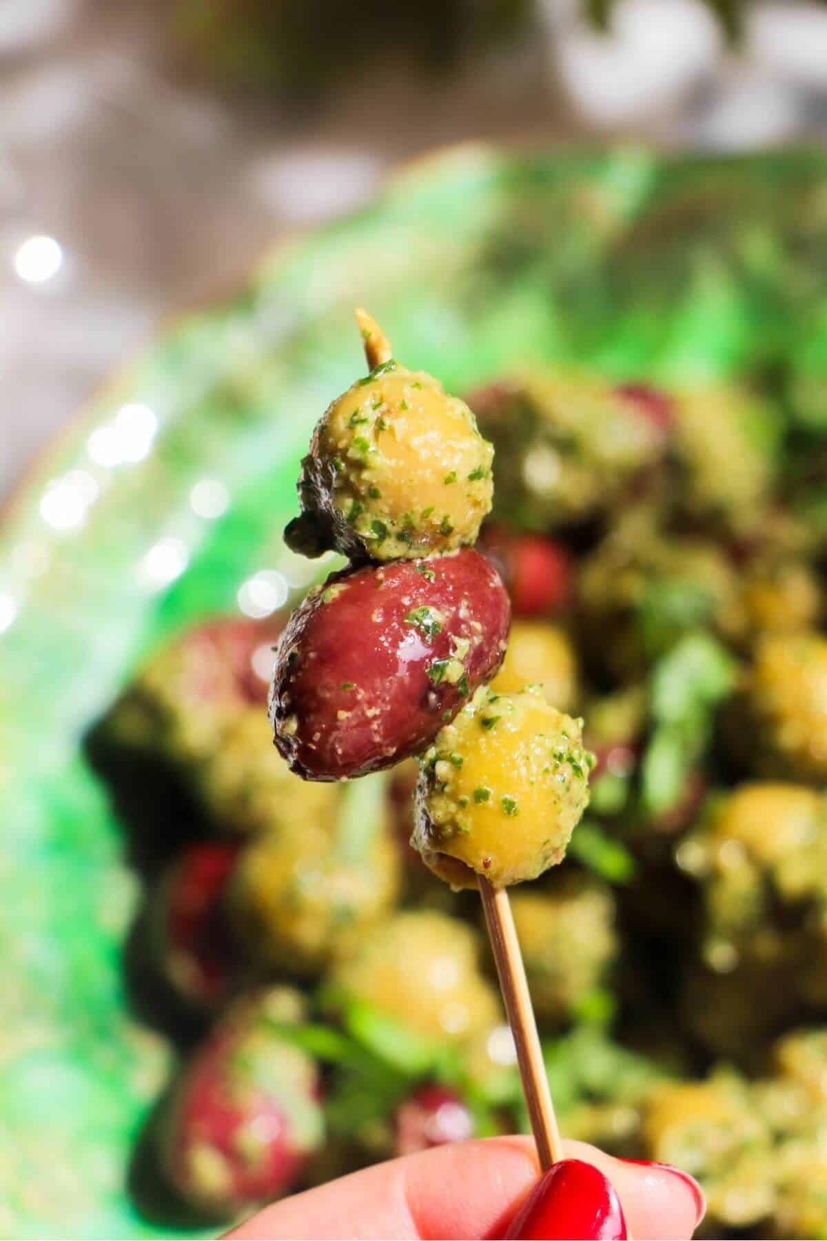 Three pesto marinated olives on a small skewer with more olives in the background.