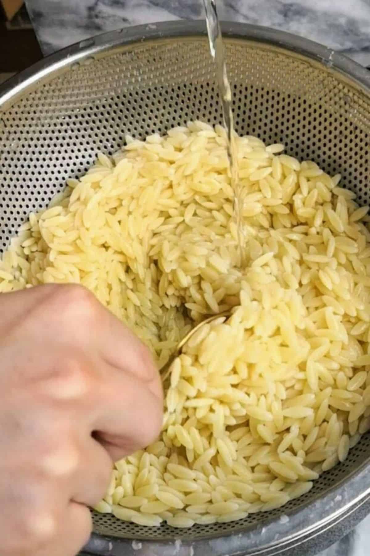 Hand stirring and rinsing cooked orzo pasta.