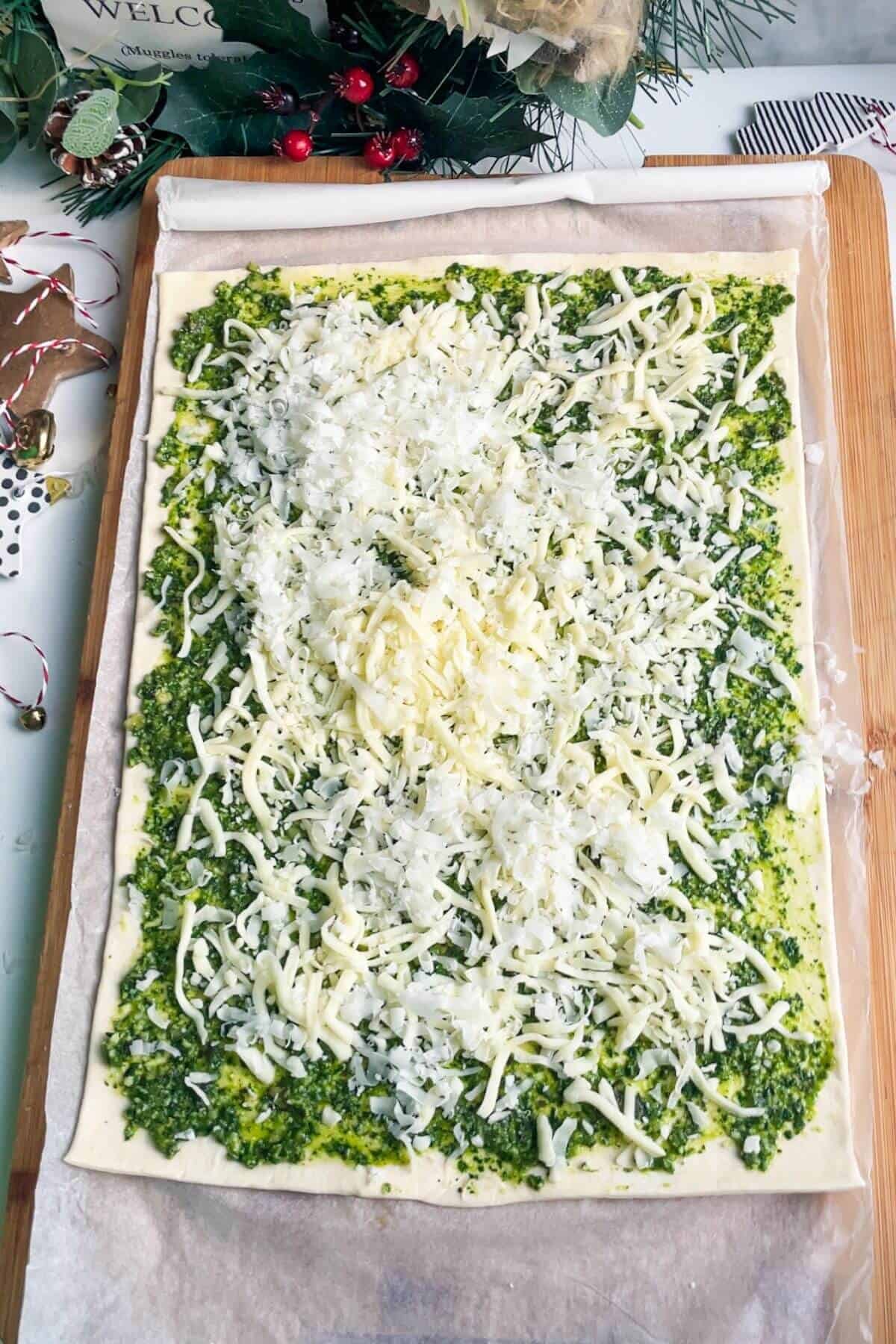 Cheese scattered over pesto on a puff pastry sheet.