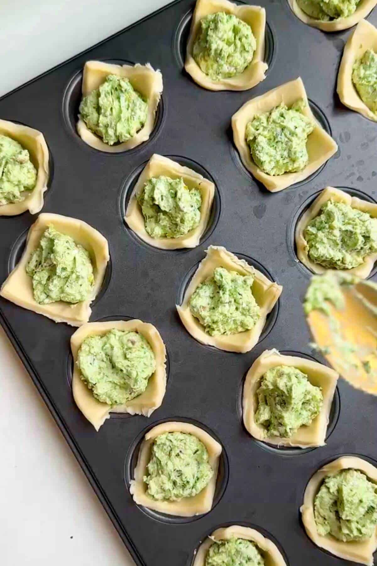 Pesto ricotta filling spooned into puff pastry cups.