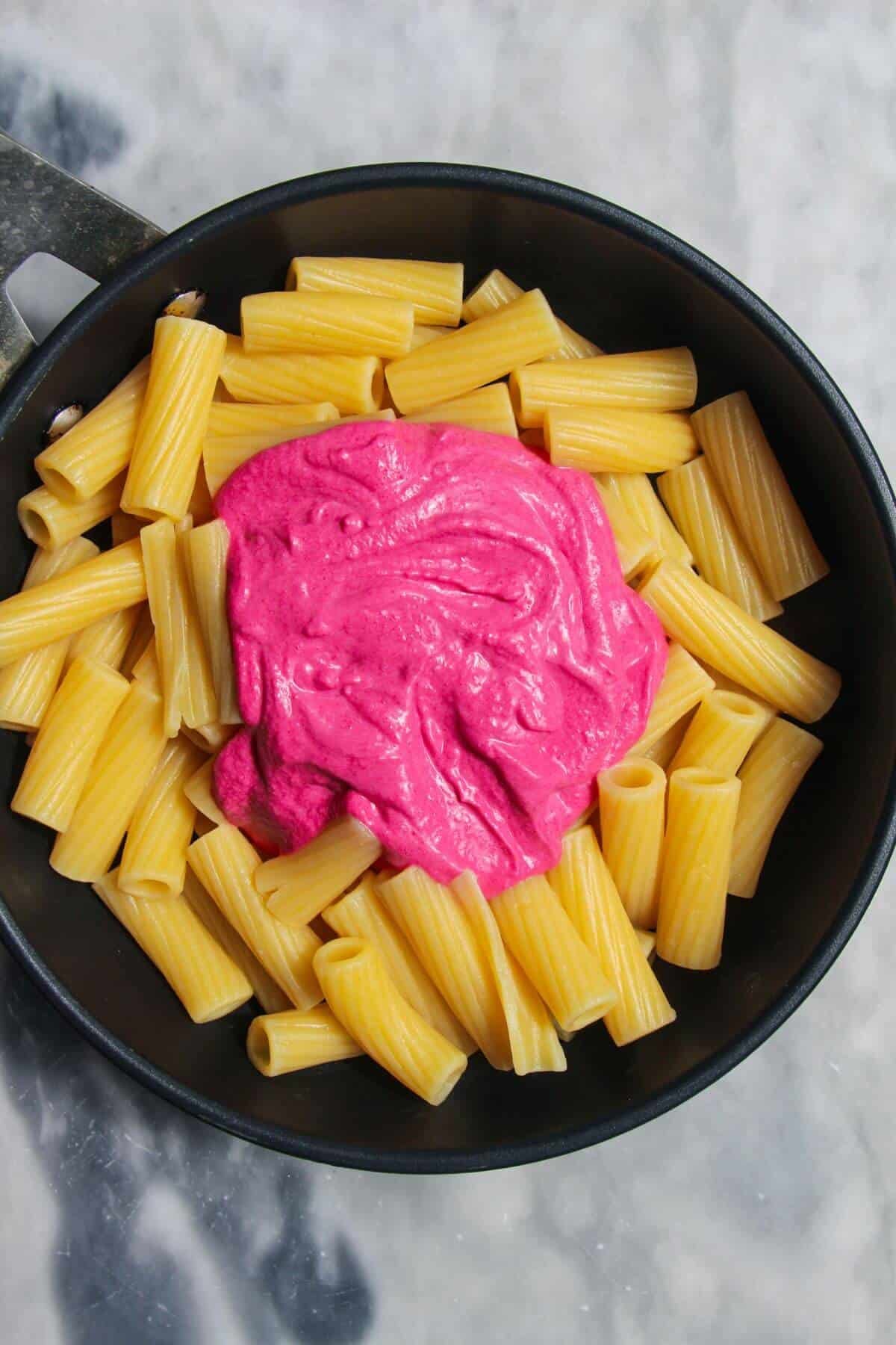 Pink sauce on top of cooked pasta in a small black pan.