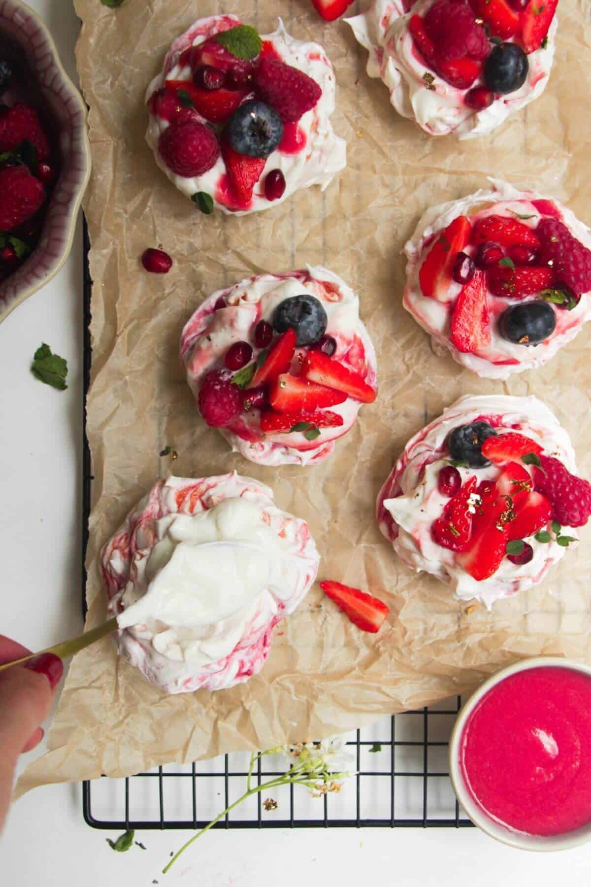 Swirling raspberry puree through cheesecake mixture on top of a mini pavlova with more mini pavlovas in the background.