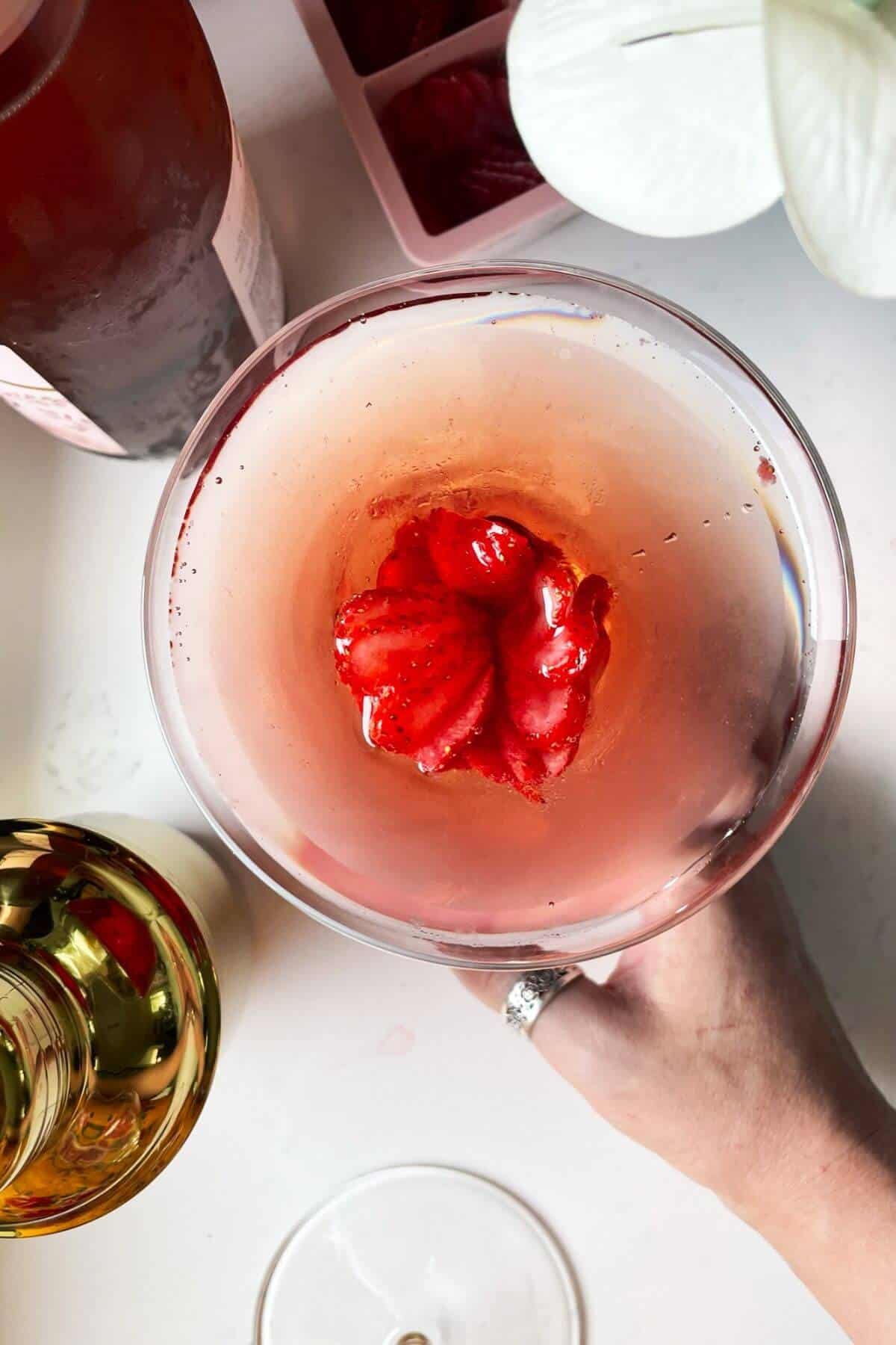 Strawberry rosé ice cube in pink gin cocktail with prosecco bottle on the side.