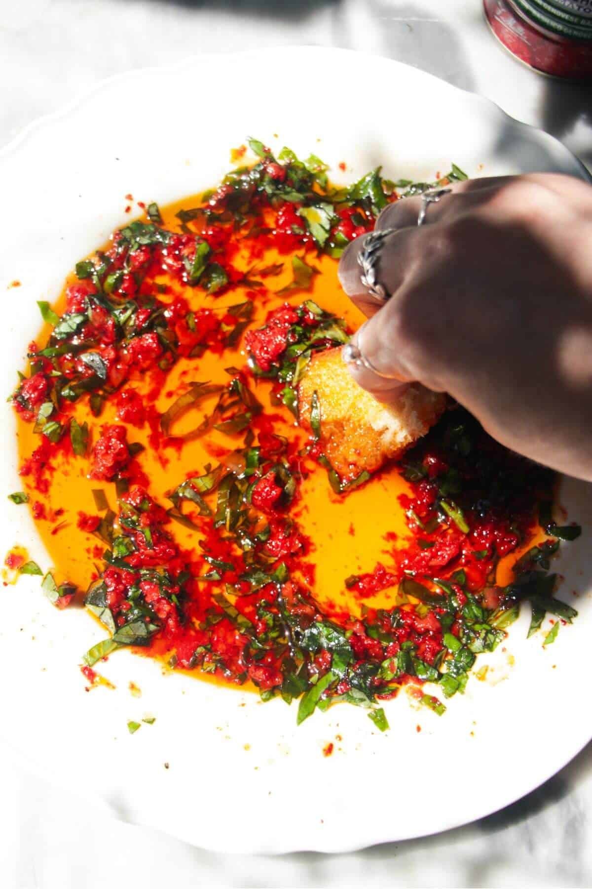 Hand swooping fresh bread through pizza dipping oil in a scalloped white plate.