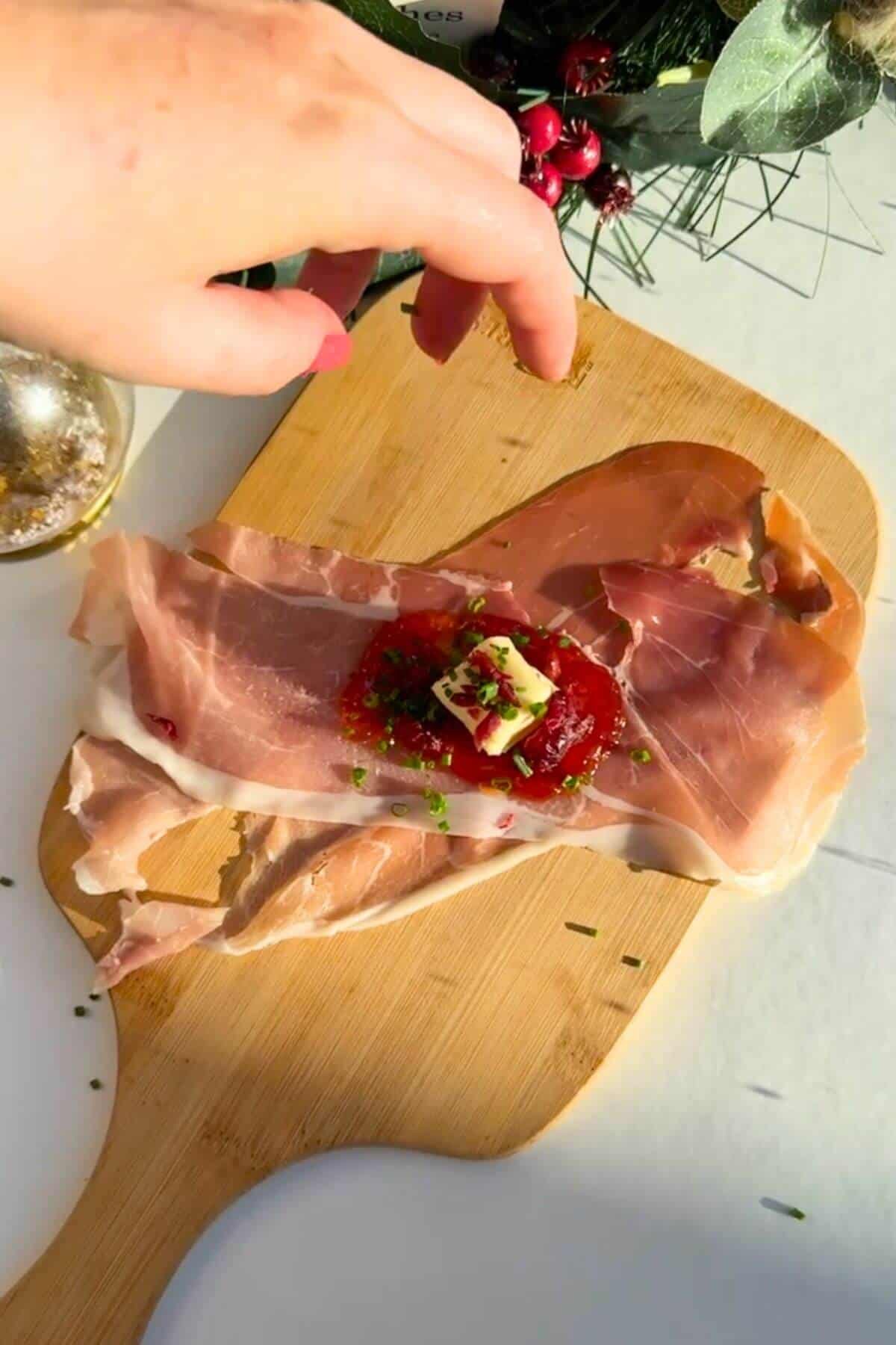 Sweet chili jam, brie and chives on top of prosciutto on wooden board.