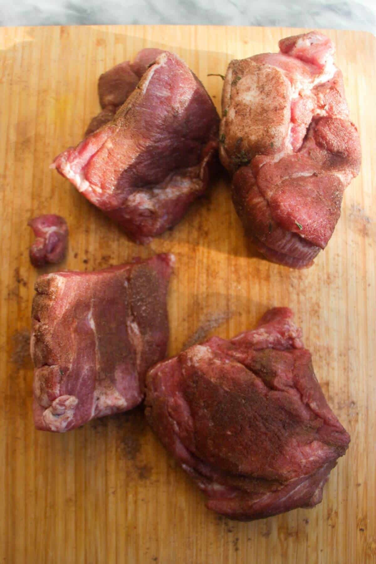 4 pieces of pork shoulder with dry rub all over it.