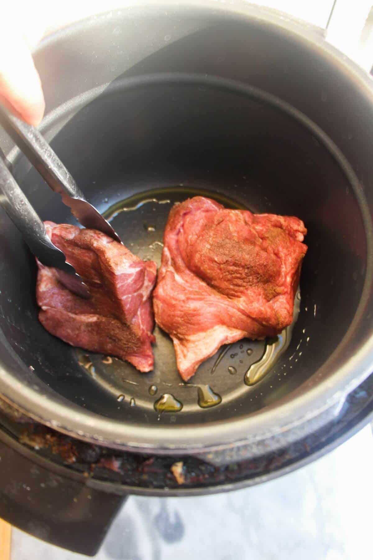 2 pieces of pork shoulder being browned in the bowl of an Instant Pot.