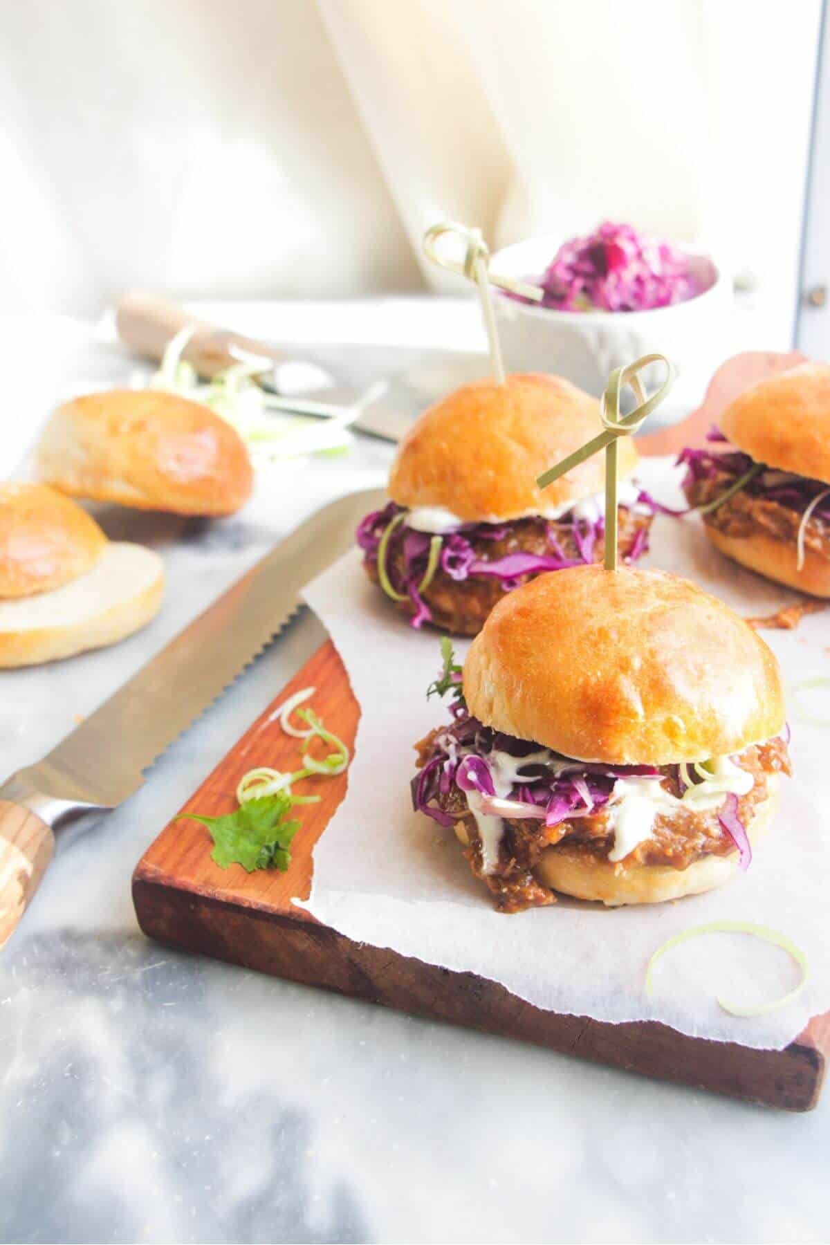 3 pulled pork sliders on a small wooden board.