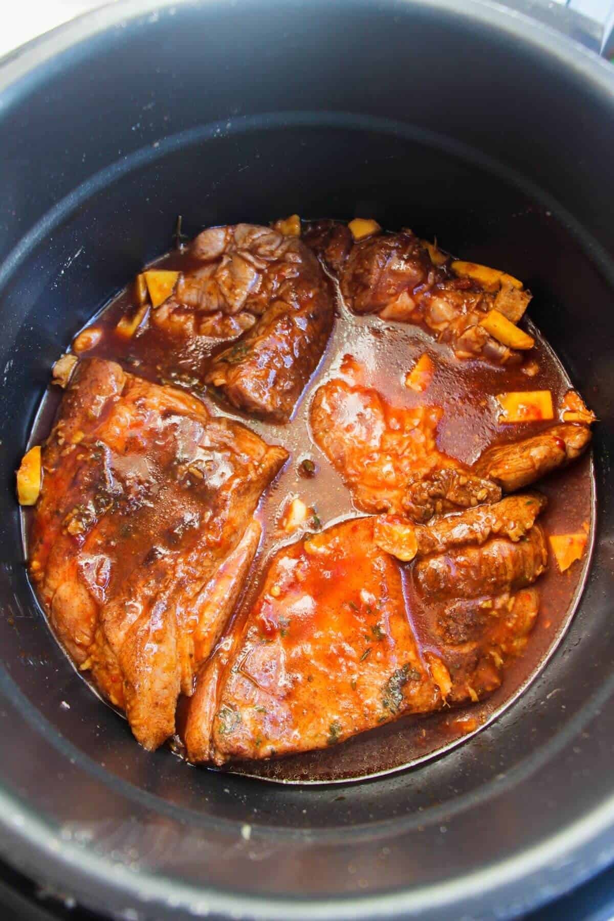 Browned pork shoulder in marinade in the bowl of an Instant Pot.