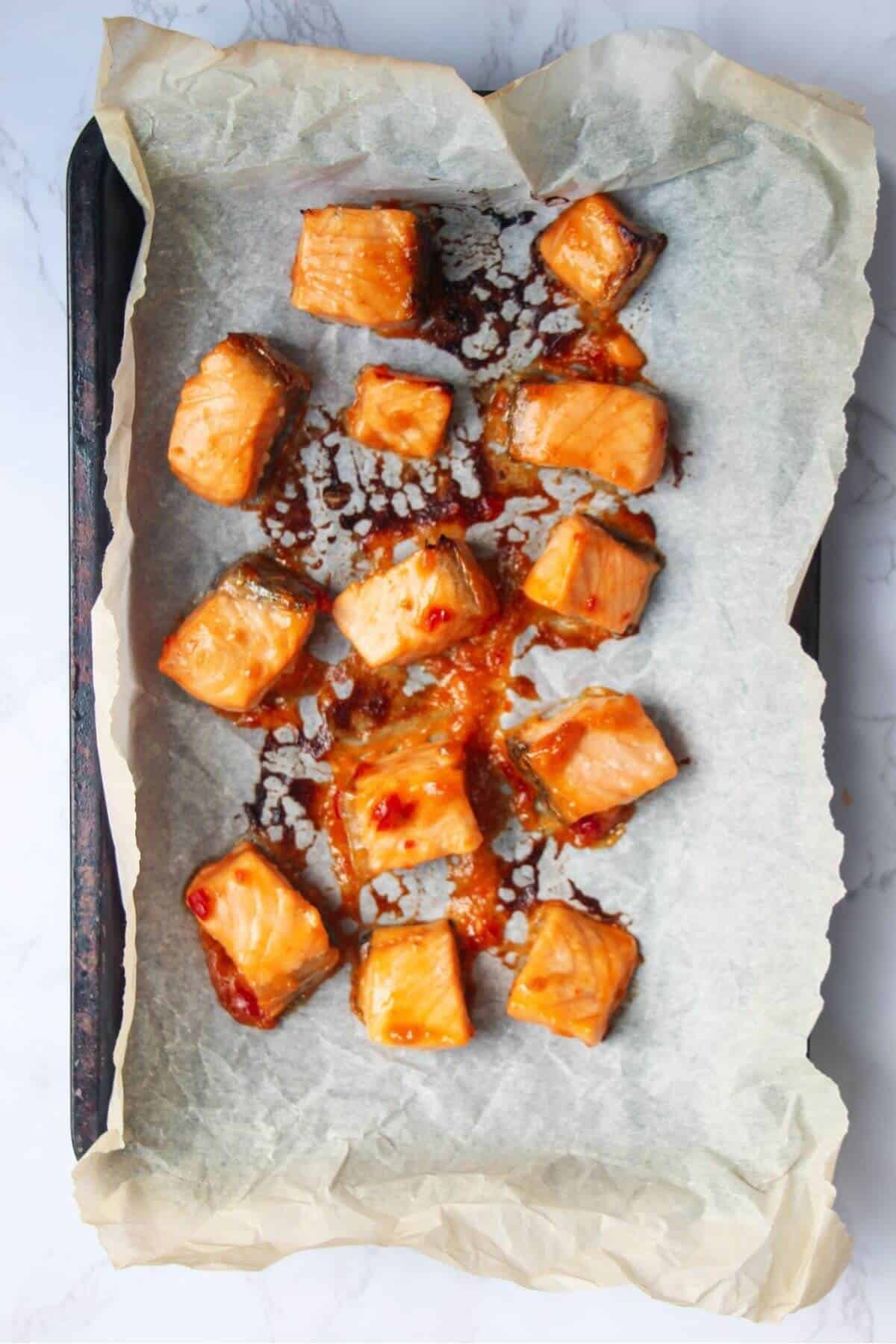 Cooked and charred salmon pieces on a lined baking tray.