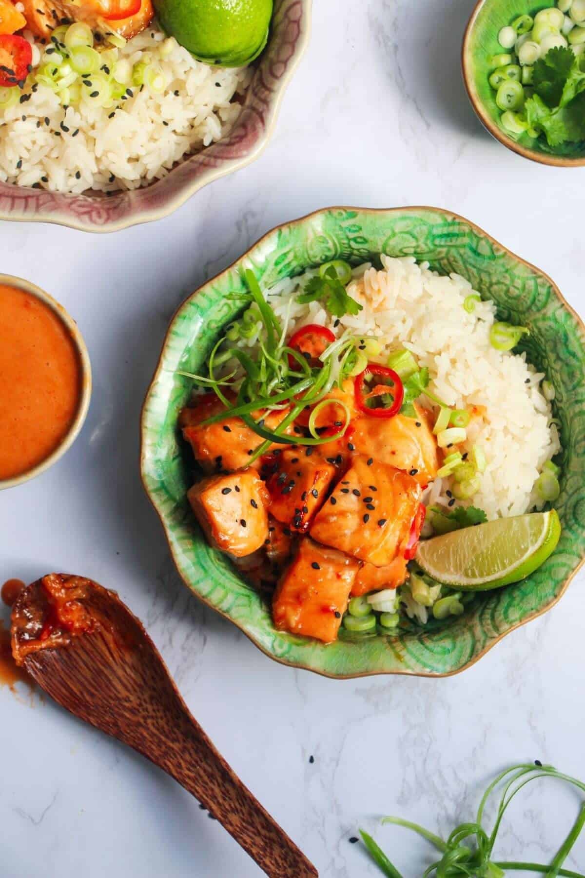 Diced charred salmon on top of rice with scallions and a lime wedge in a small green bowl, with another bowl in the background.