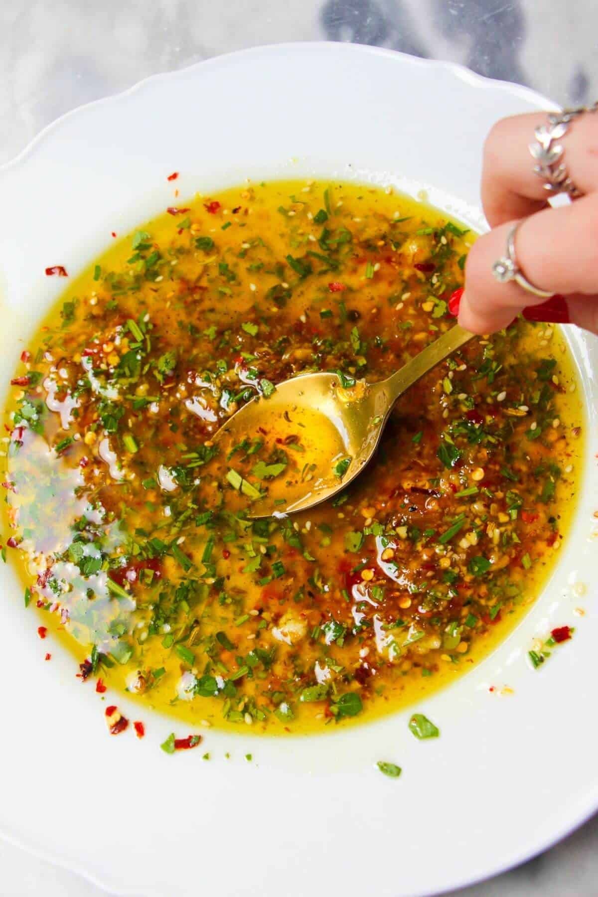 Gold spoon mixing feta marinade ingredients in a white scallop edged plate.
