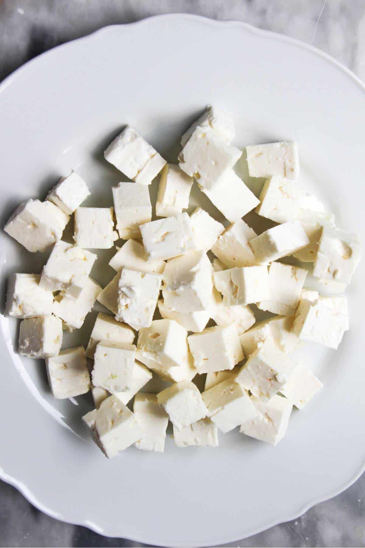Diced feta on a white scalloped plate.