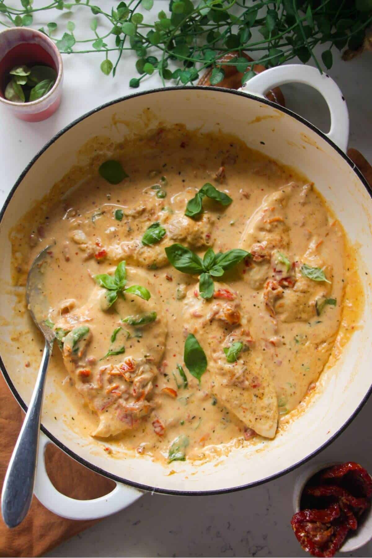 Chicken breasts in creamy sundried tomato sauce in a large white skillet.