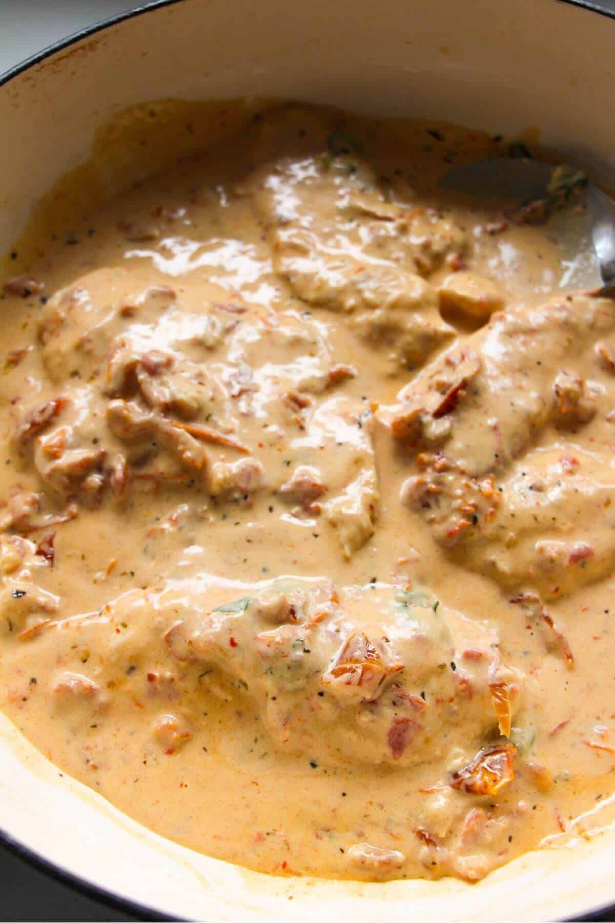 Cooked chicken breasts added back into creamy sundried tomato sauce in a large white skillet.
