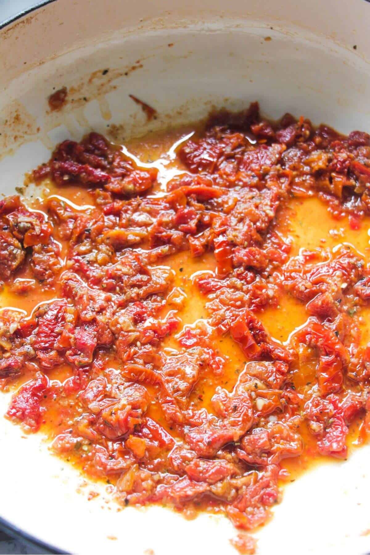 Chopped sundried tomatoes cooking in a large white skillet.