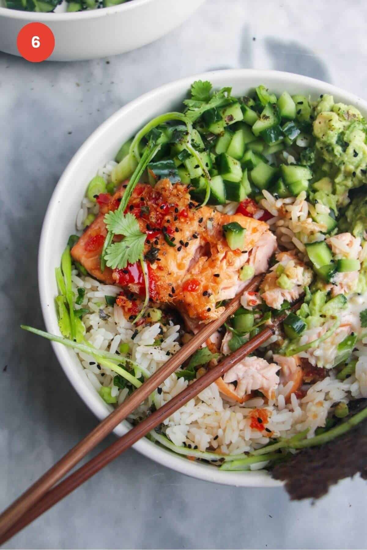 Salmon on top of rice with cucumber and avocado in a small bowl.