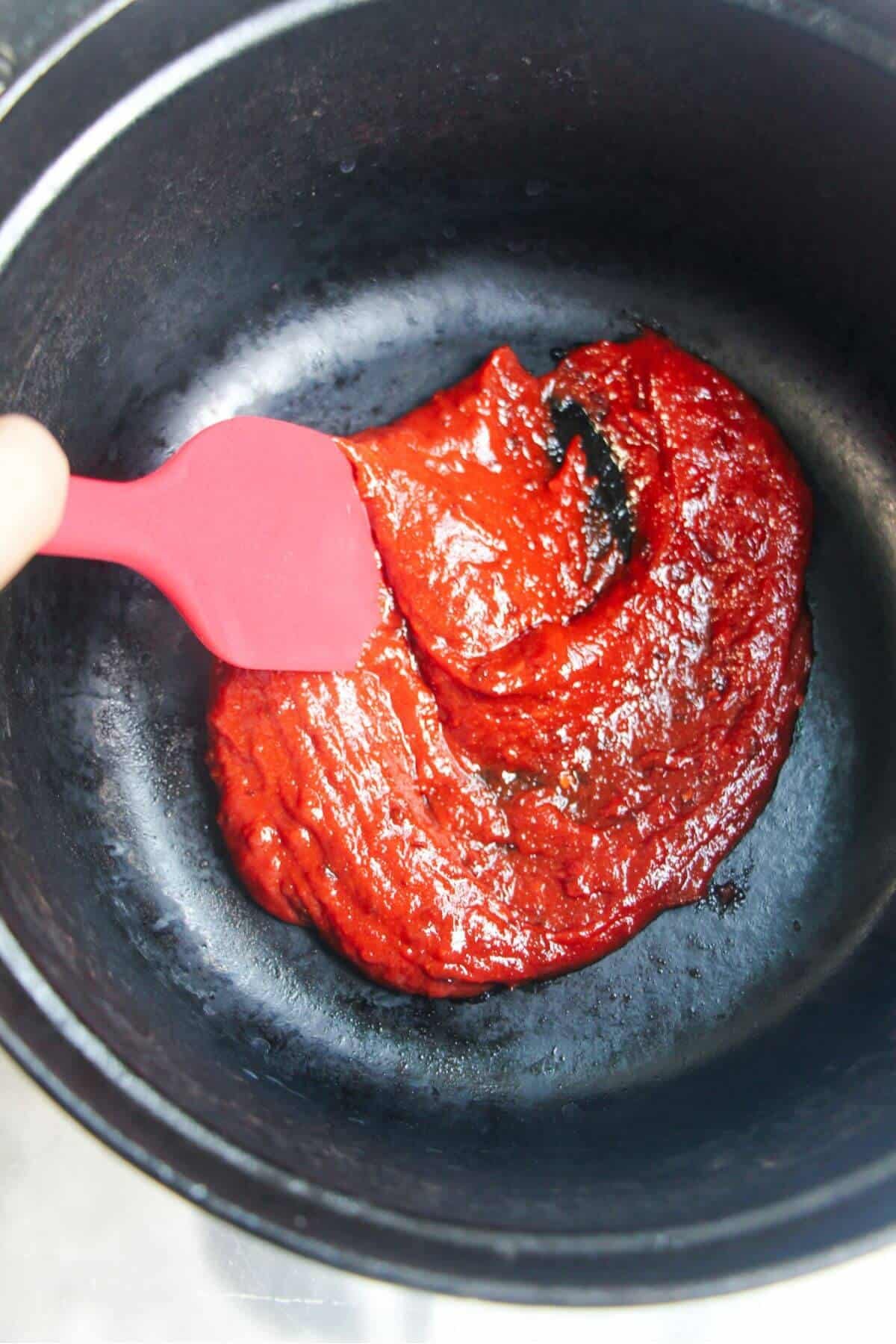 Red paste in a large black pot, stirred with a red spatula.