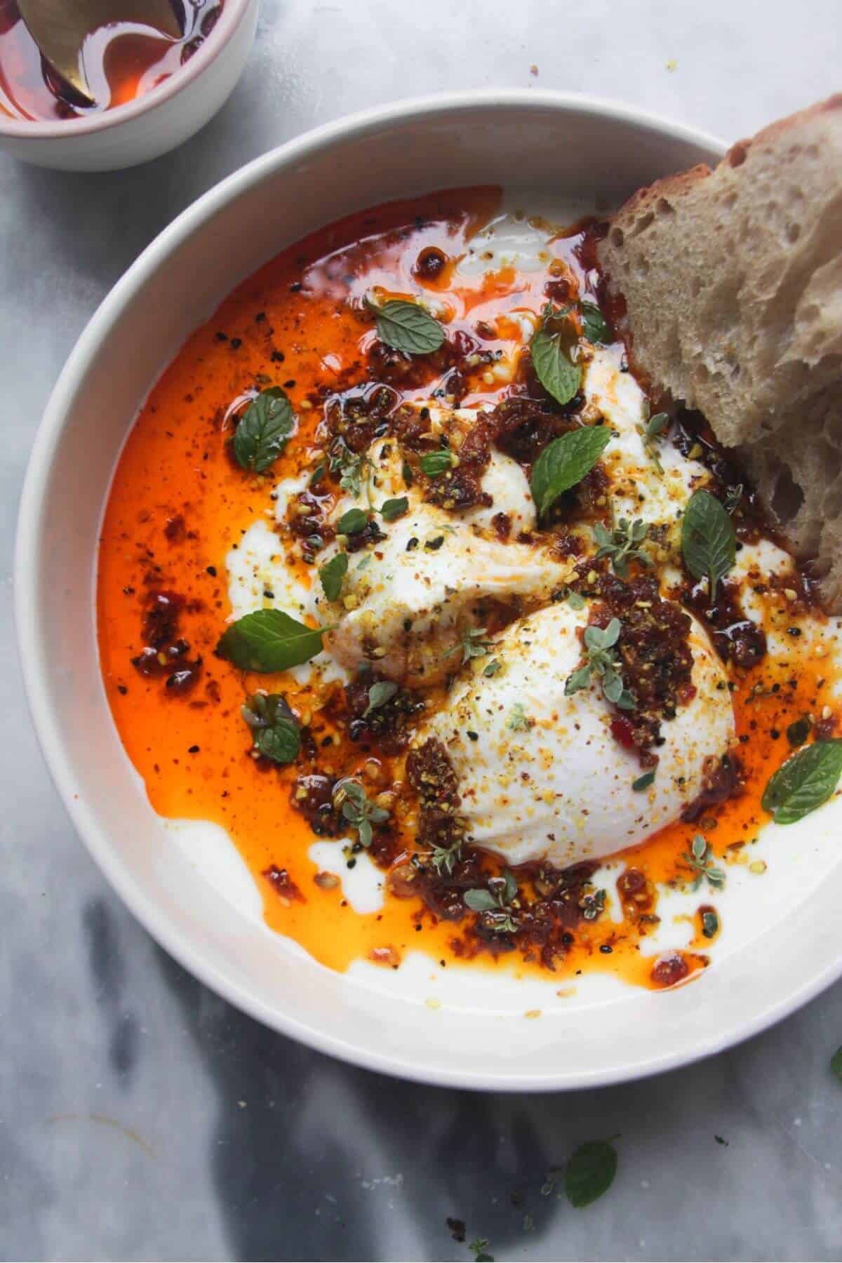Poached eggs with chilli oil and garlick yogurt in a small white bowl with toast on the side.