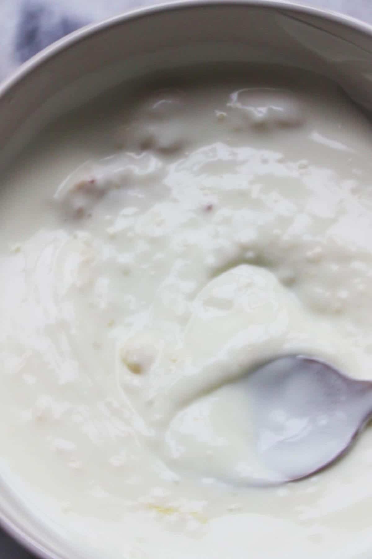 Small spoon mixing crushed garlic through yogurt in a small white bowl.