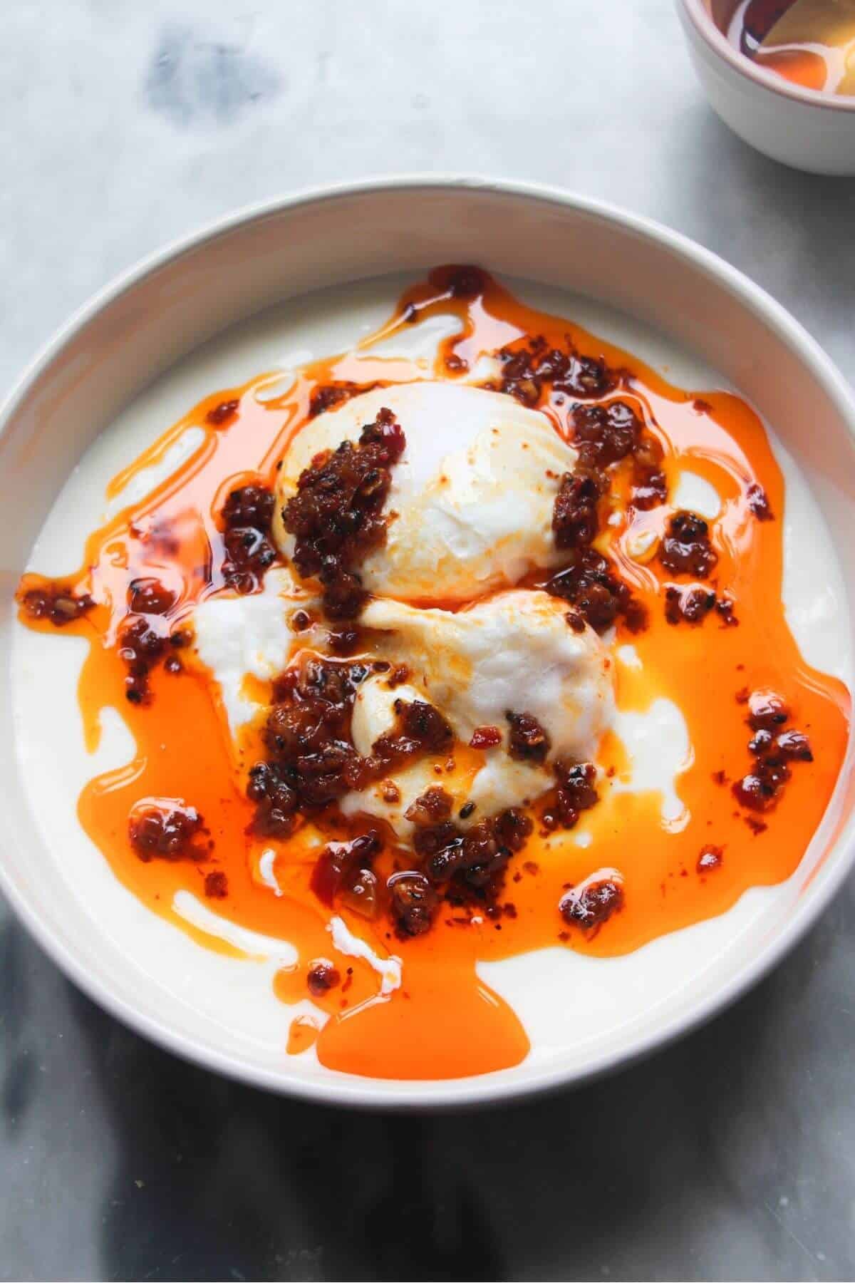 Chilli oil drizzled on top of 2 poached eggs sitting in a small bowl of yogurt.