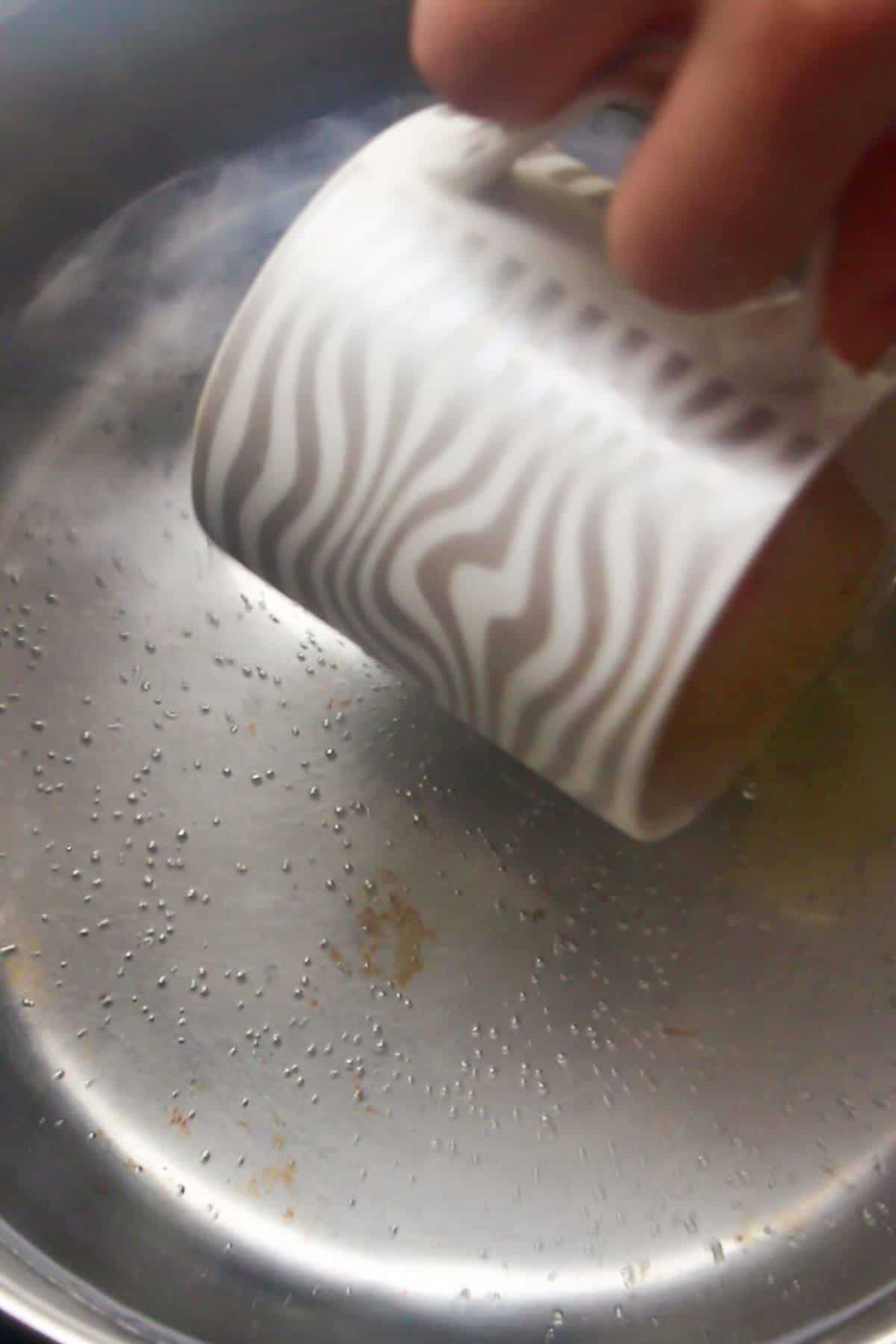 Small cup pouring an egg into simmering water in a silver pot.