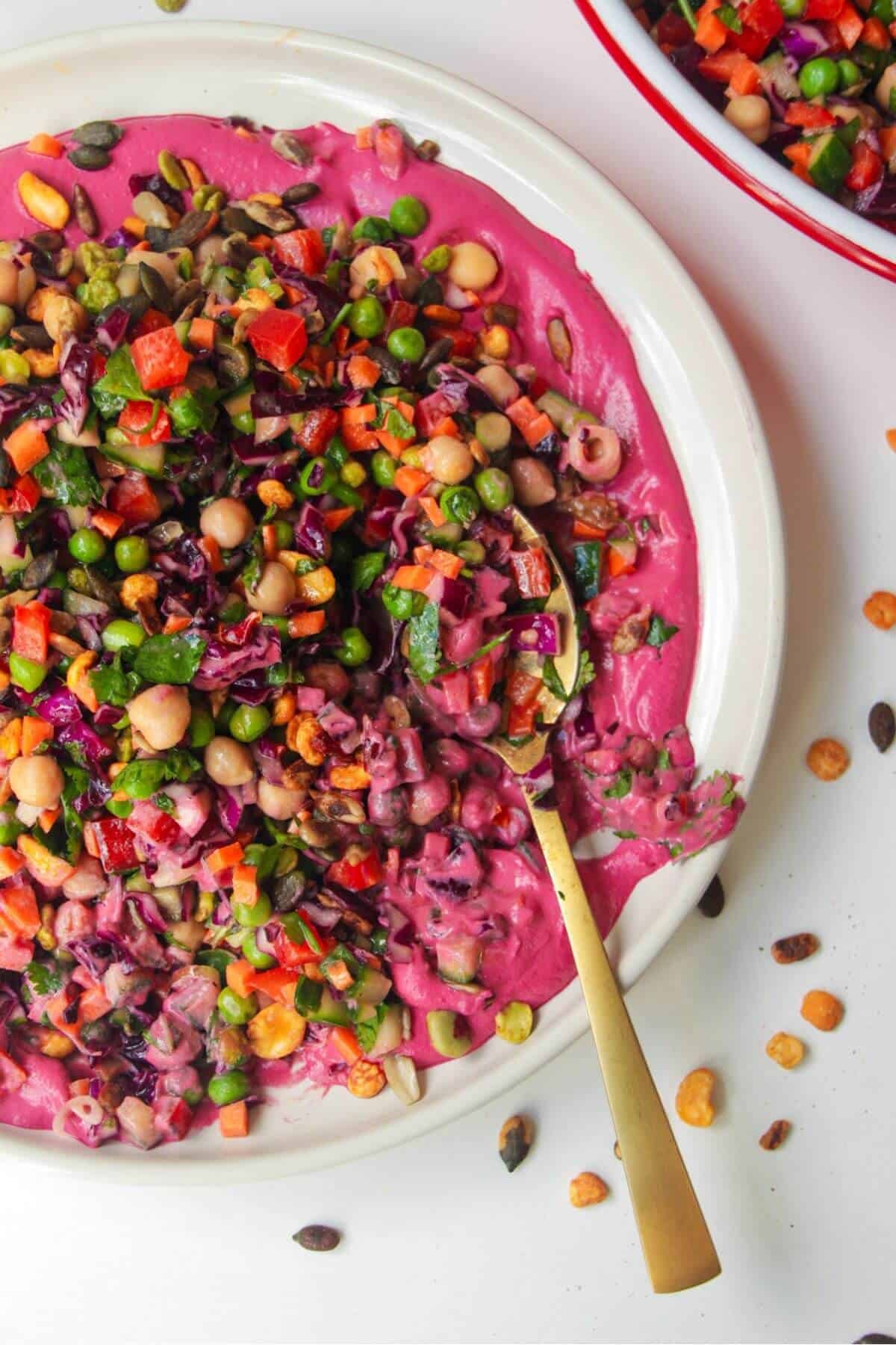 Rainbow chopped salad on pink tahini sauce on a white plate, with extra sauce on the side.