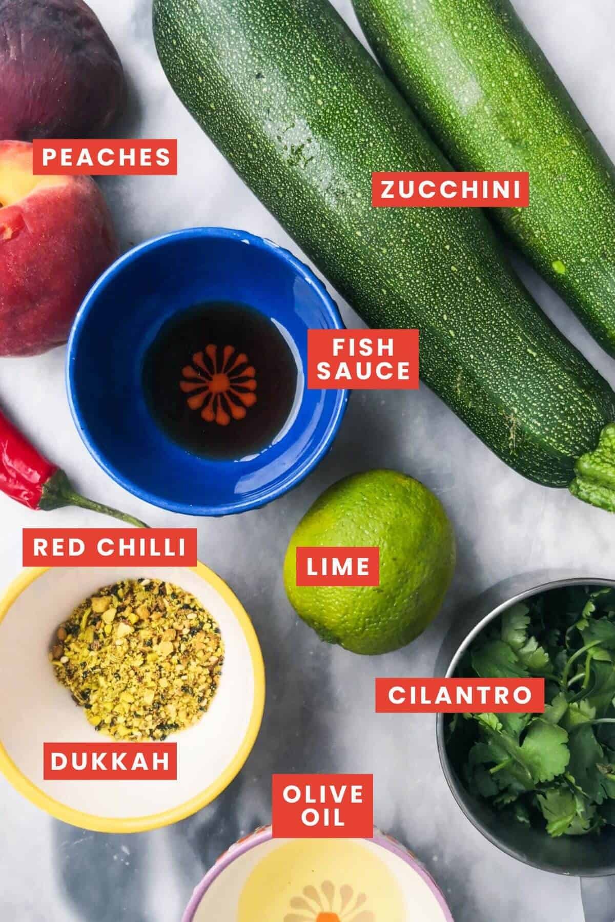 Ingredients for raw zucchini salad laid out on a grey marble background and labelled.
