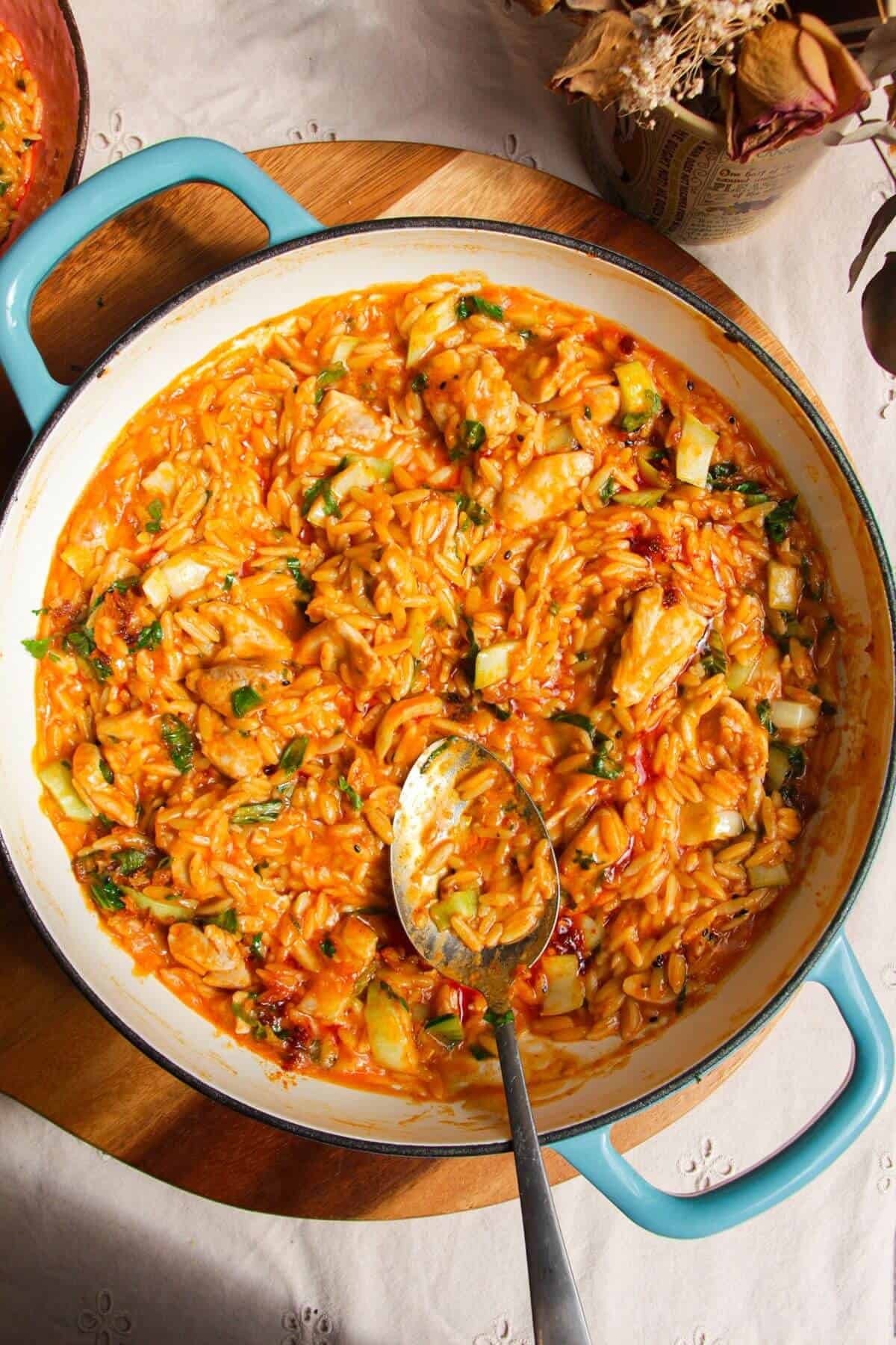 Red curry chicken orzo in a pan with a spoon.