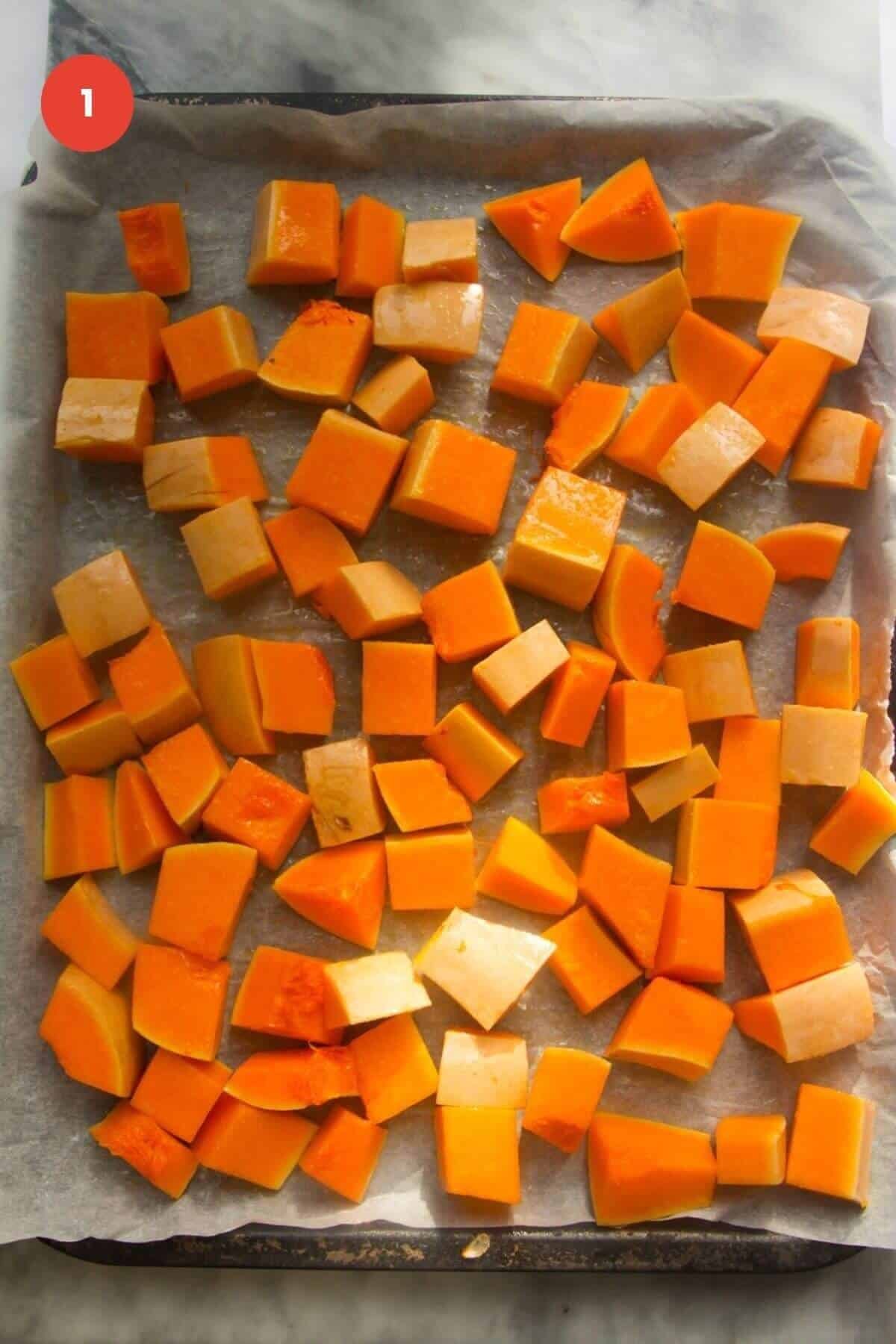 Diced butternut squash laid out on a lined oven tray.