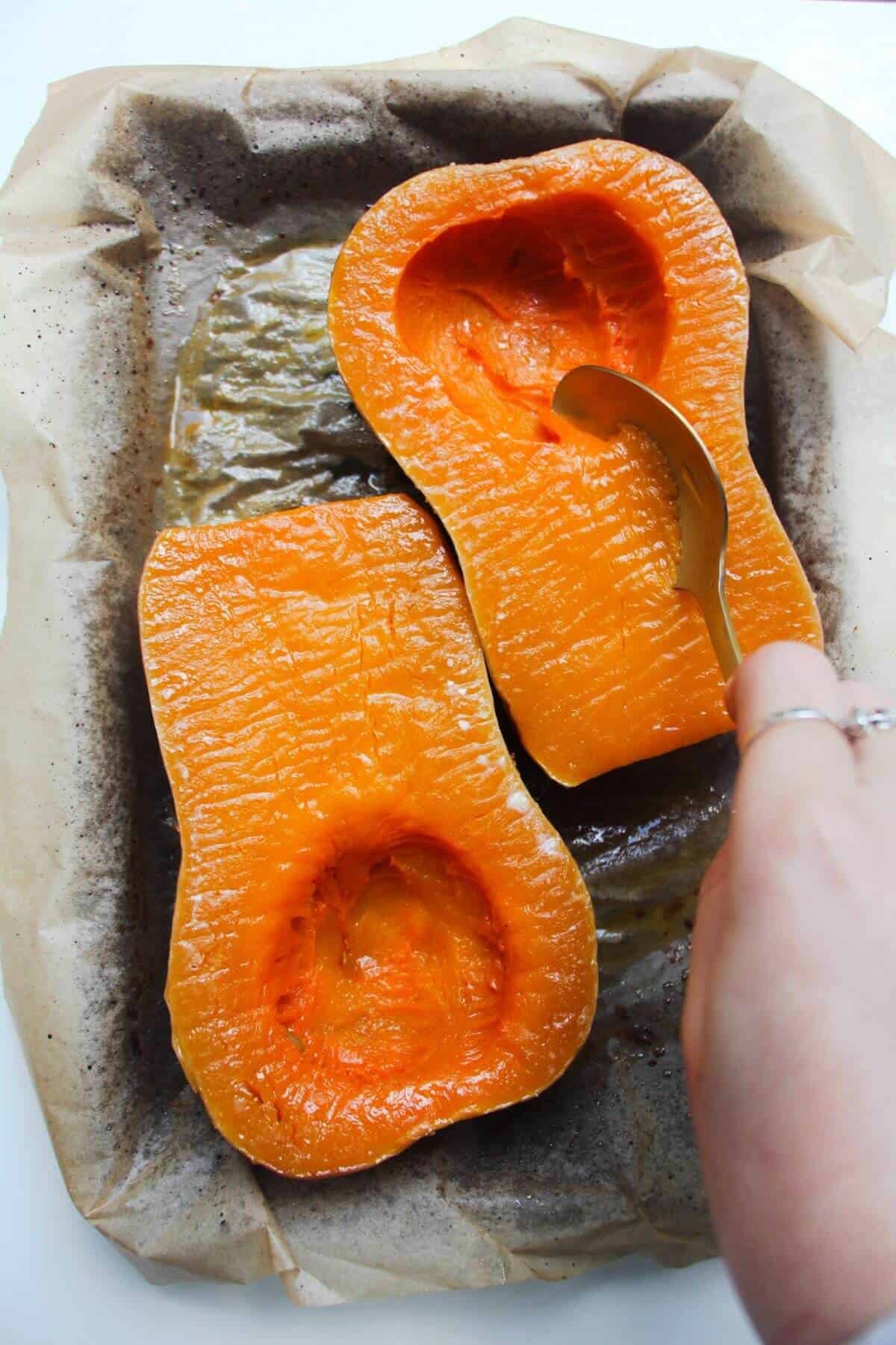 Scooping soft roasted flesh from squash skin.