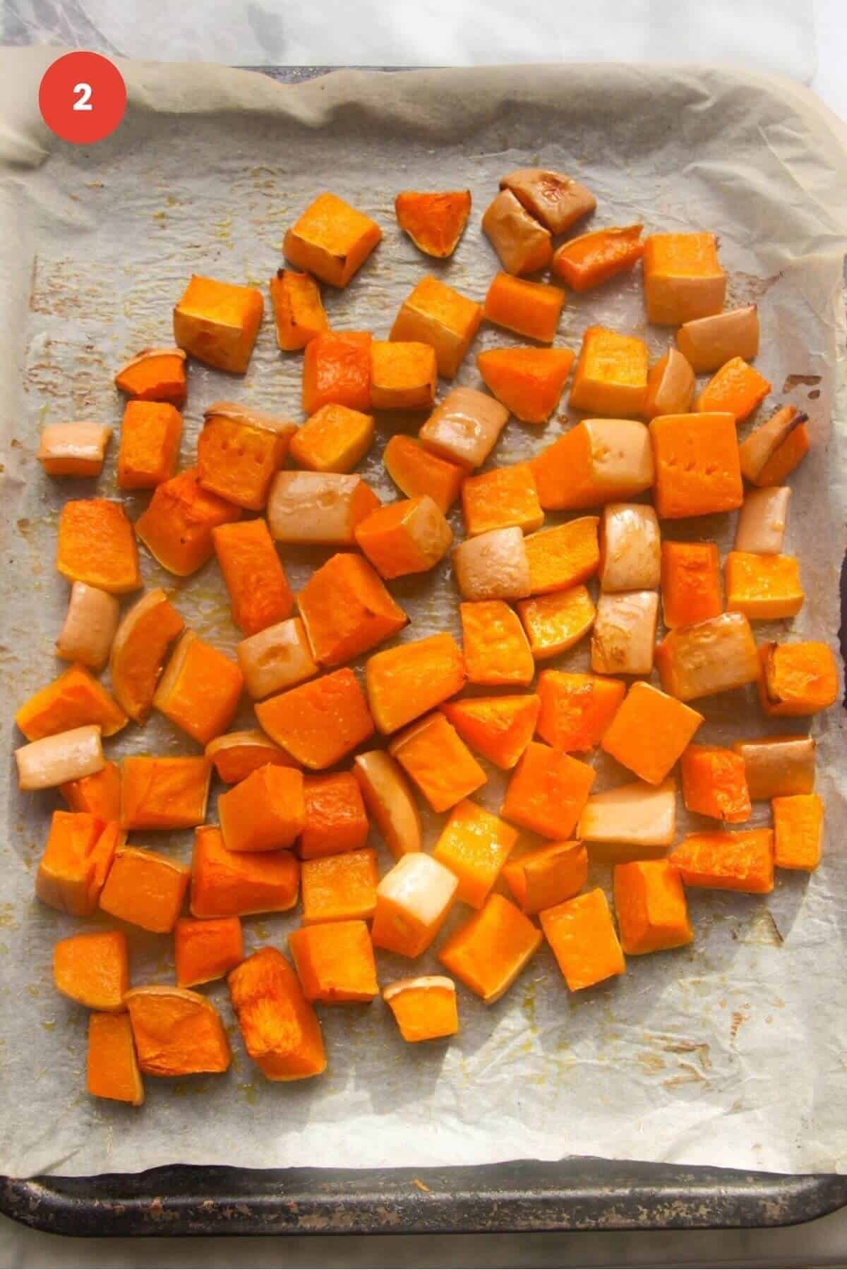 Charred, roasted butternut squash cubes on a lined oven tray.