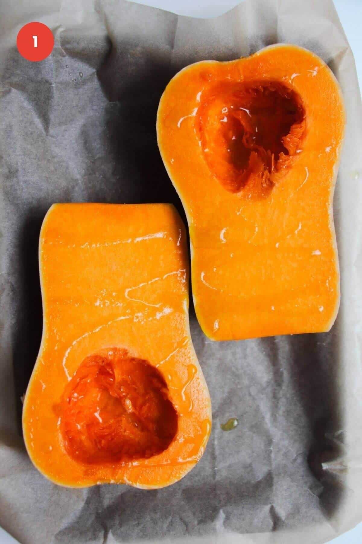 Two butternut squash halves on a lined tray, drizzled with olive oil.
