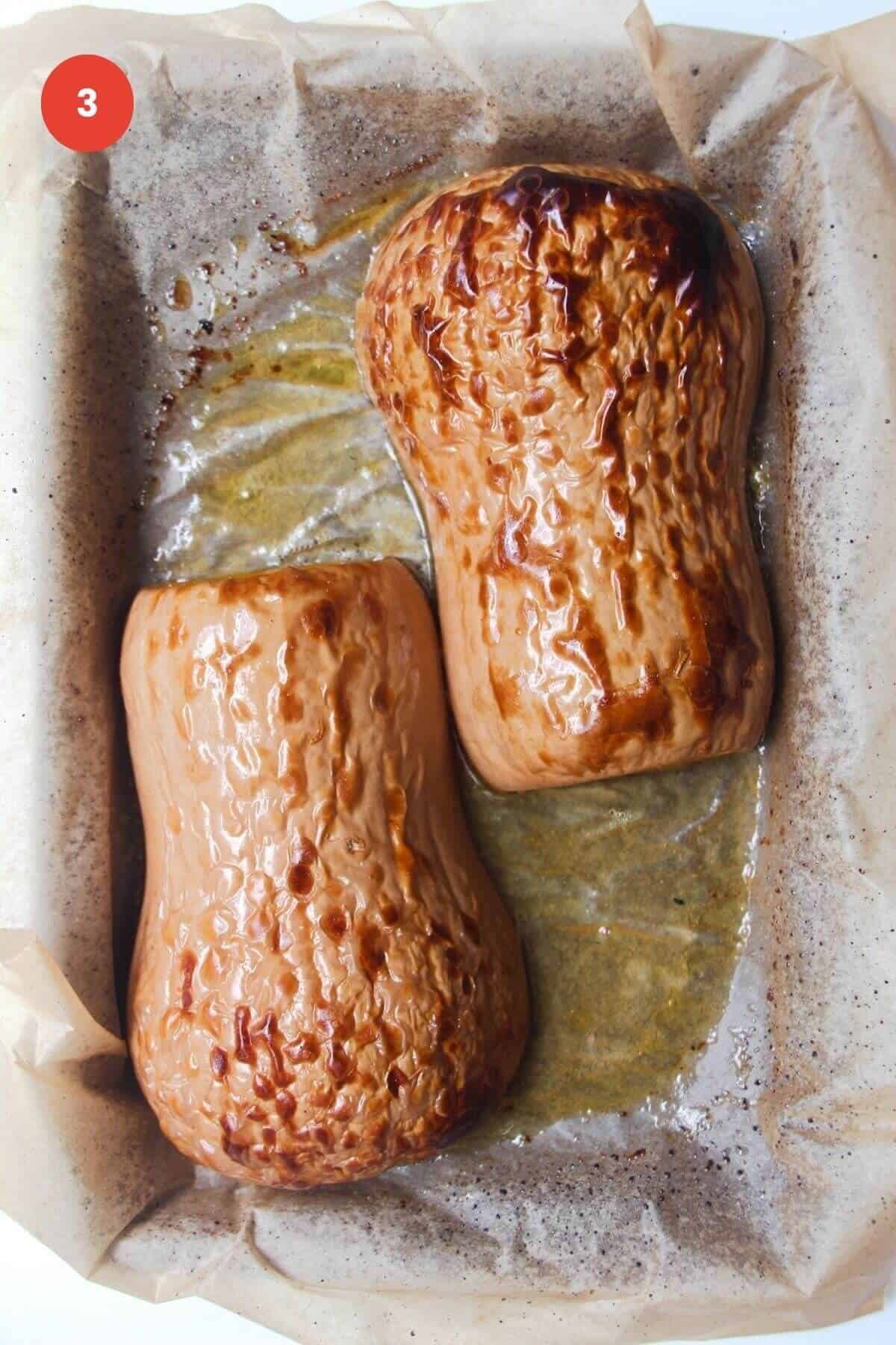 Charred, roasted butternut squash halves upside down on an oven tray.