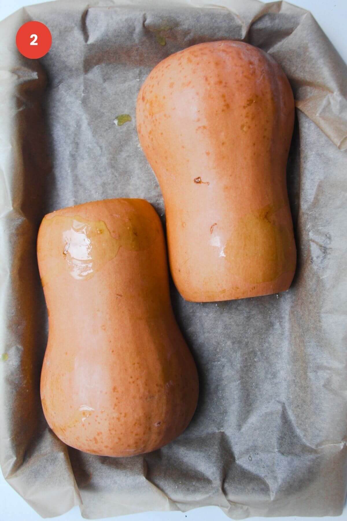 Two butternut squash halves upside down on an oven tray.