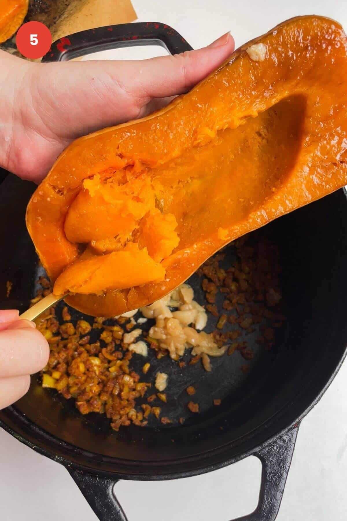 Spoon scooping butternut squash flesh into pot.