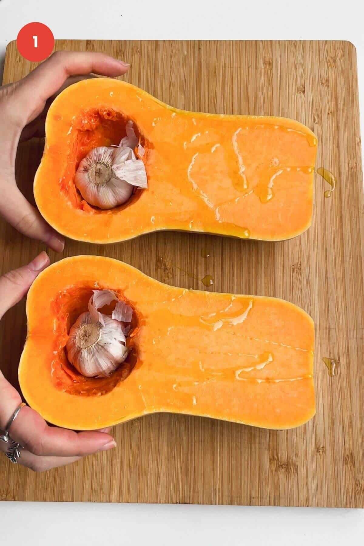 Halved butternut squash with garlic bulbs on lined oven tray.