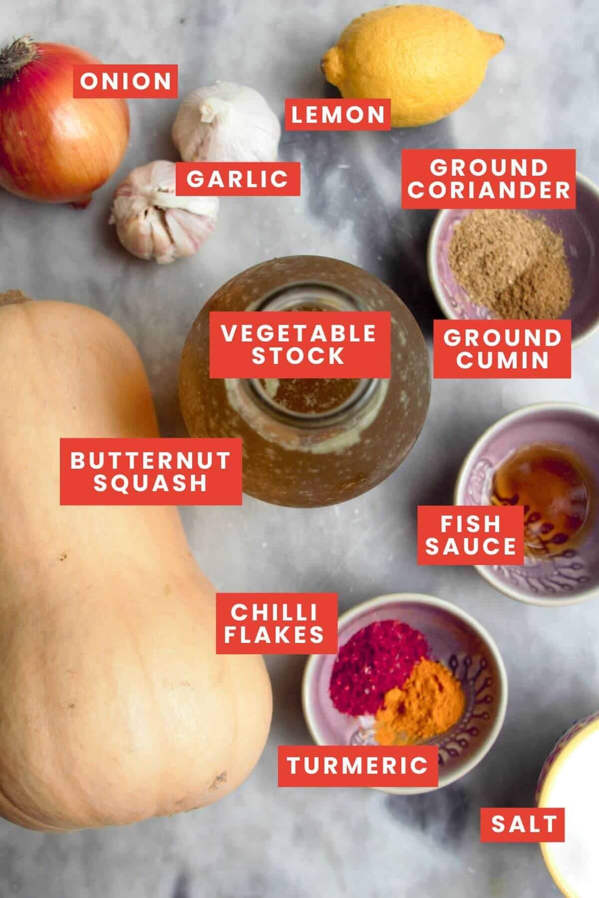 Ingredients for butternut squash soup laid out on a marble background and labelled.