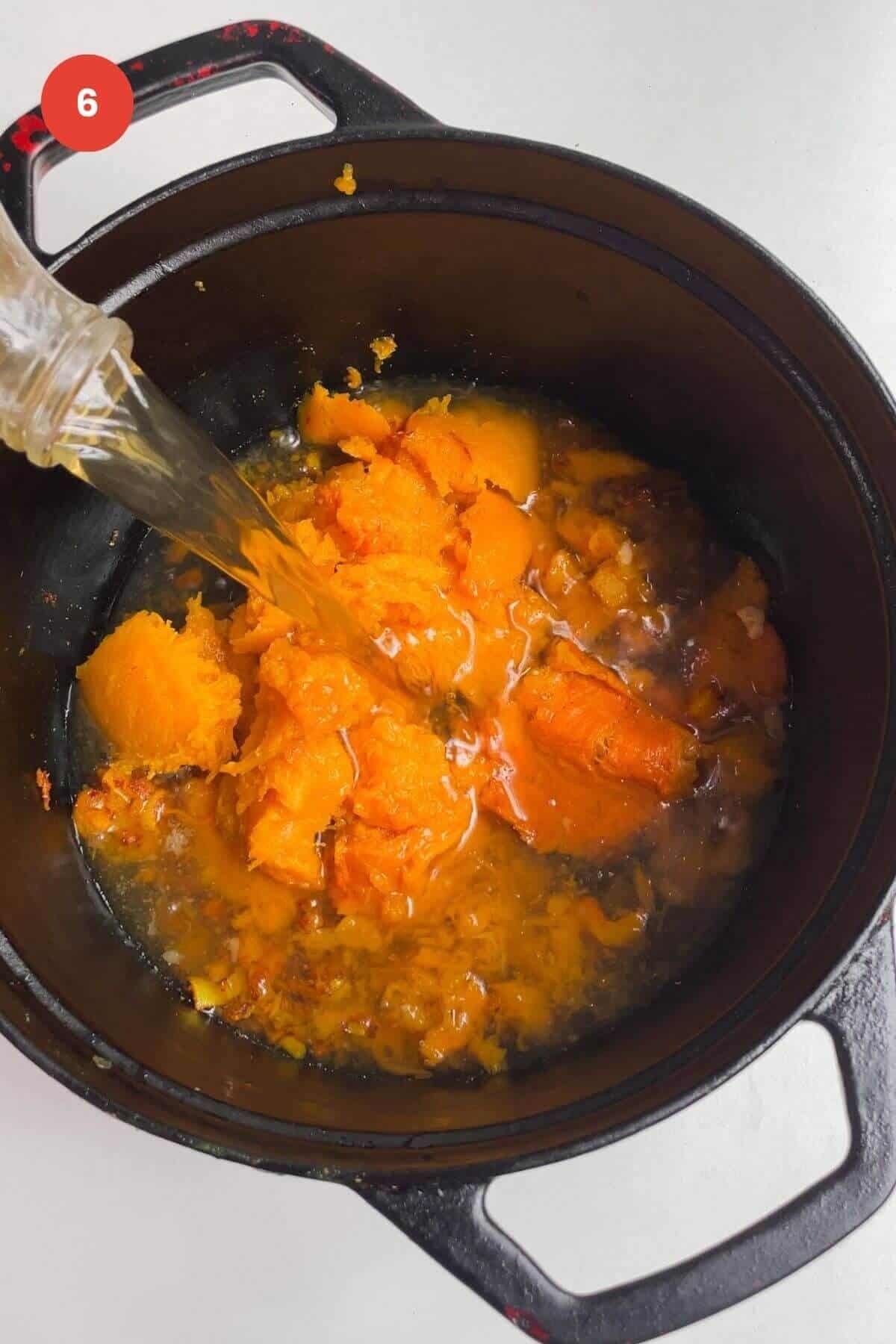 Pouring stock into butternut squash soup in pot.