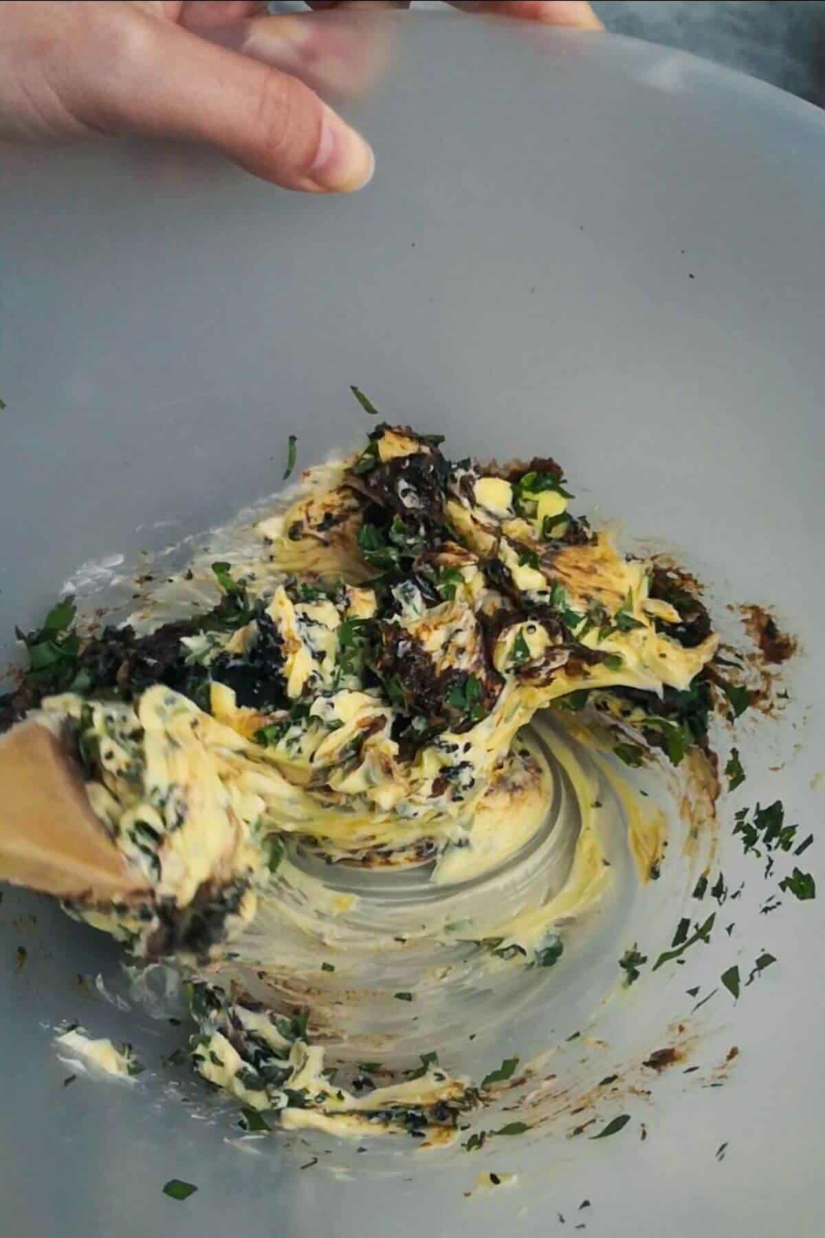 Large wooden spoon starting to mix the roasted garlic butter in a large mixing bowl.