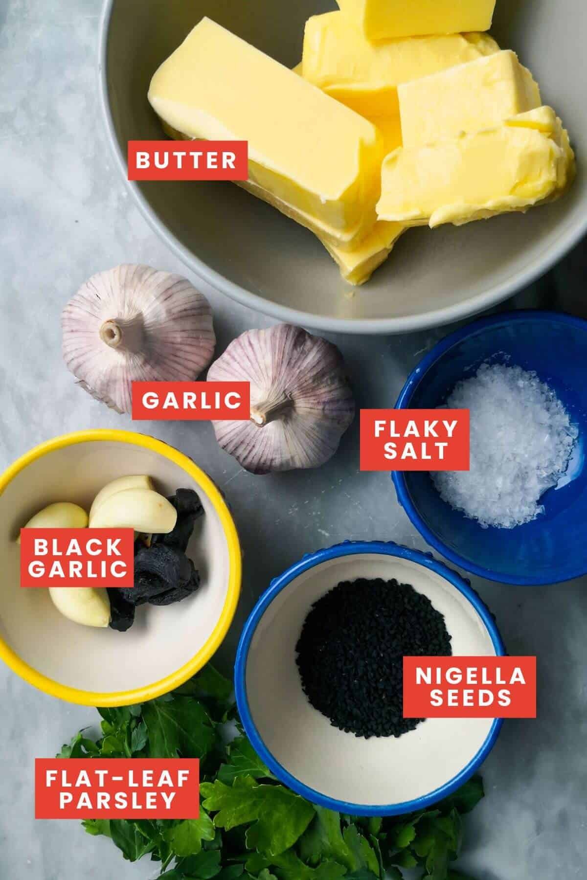 Roasted garlic butter ingredients in small bowls on a grey marble background.